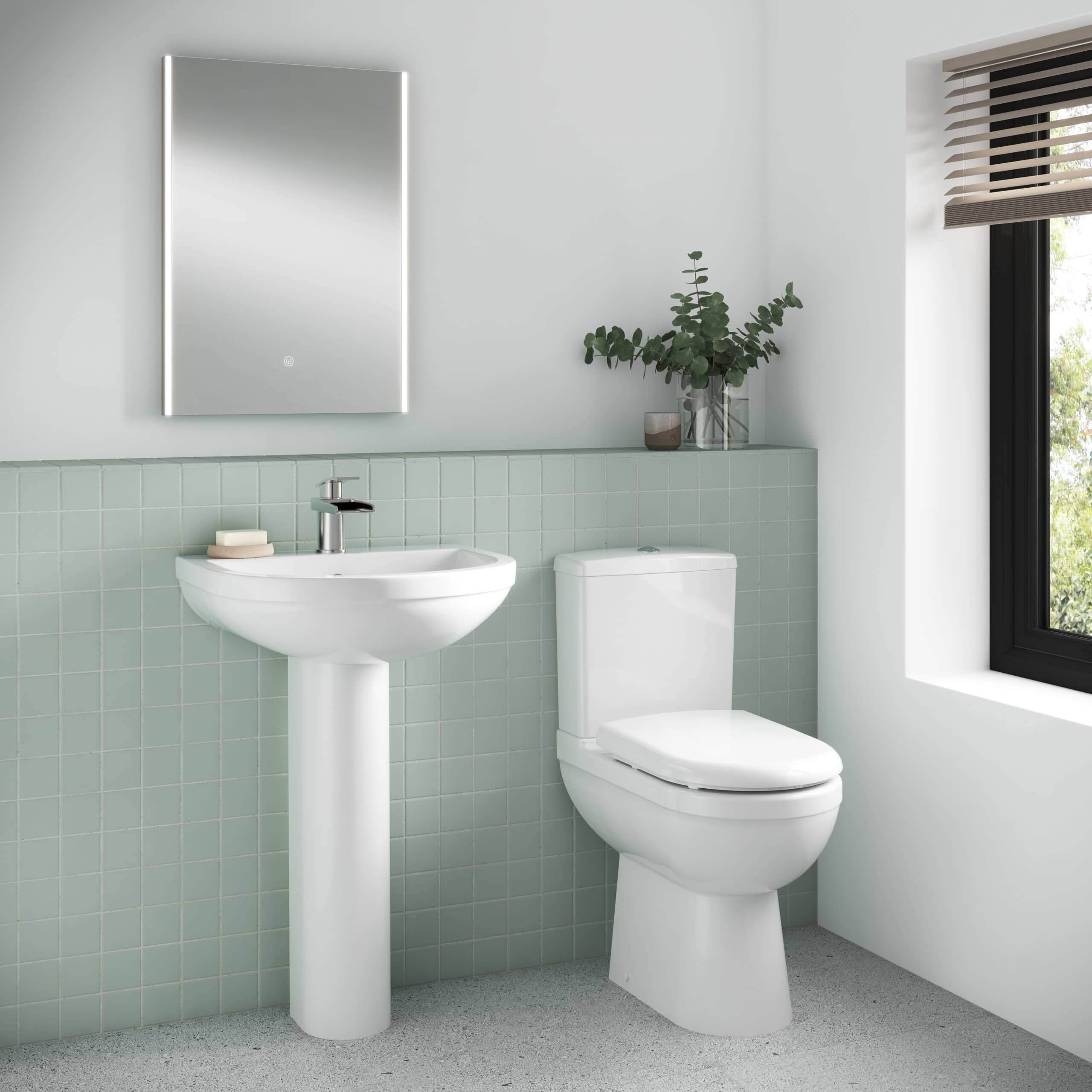 Modern white bathroom sink and toilet with green tiled wall, minimalist mirror and natural light for contemporary bathroom design.