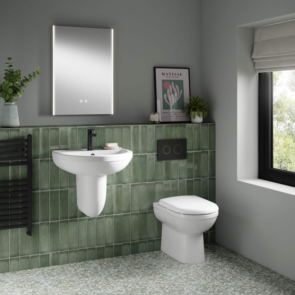 Modern bathroom with green tiled wall, white toilet and sink, black fixtures, decorative plants, framed art, and large window providing natural light, showcasing stylish and functional bathroom design.