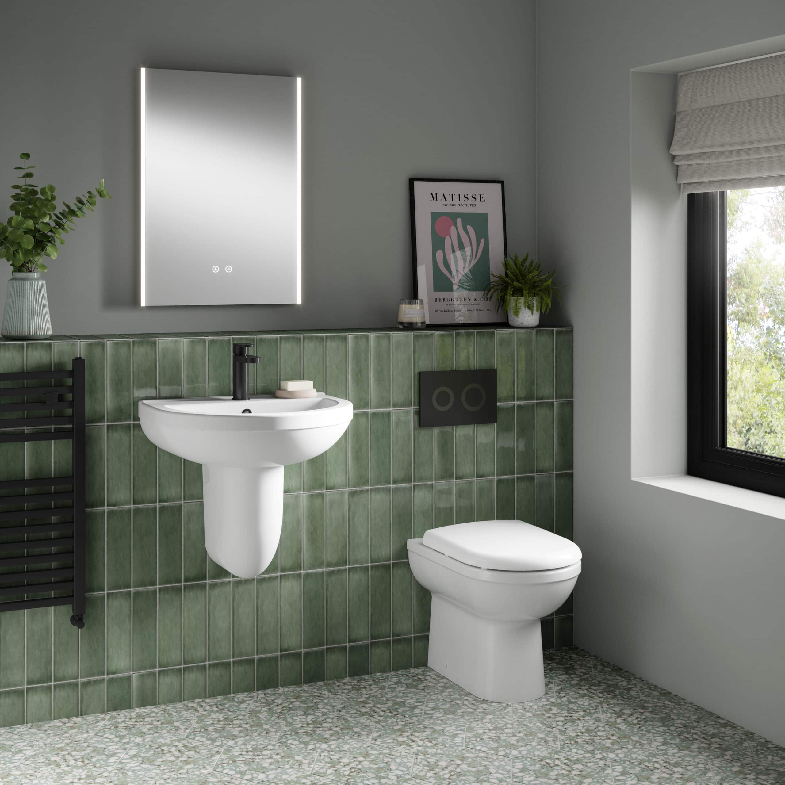 Modern bathroom with green tiled wall, white toilet and sink, black fixtures, decorative plants, framed art, and large window providing natural light, showcasing stylish and functional bathroom design.