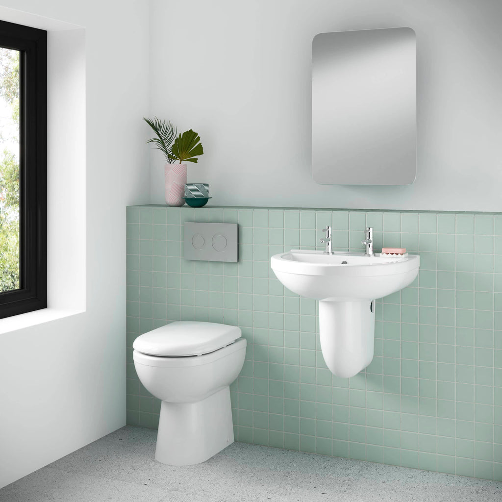 Sleek white bathroom with wall-mounted toilet and pedestal sink, featuring modern chrome fixtures, pastel green tiling, and stylish decor for a minimalist and contemporary look.