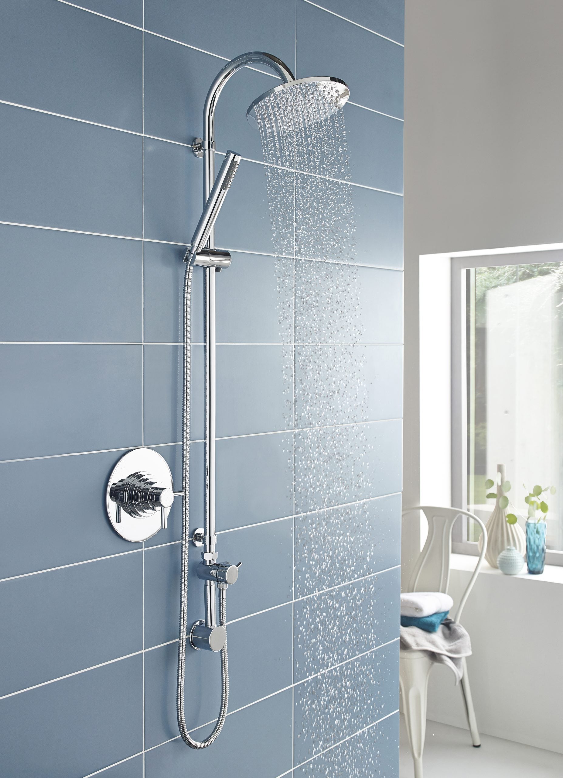 Shower head and hand shower in a modern bathroom with blue tiled wall, chrome fixtures, and bright natural light.