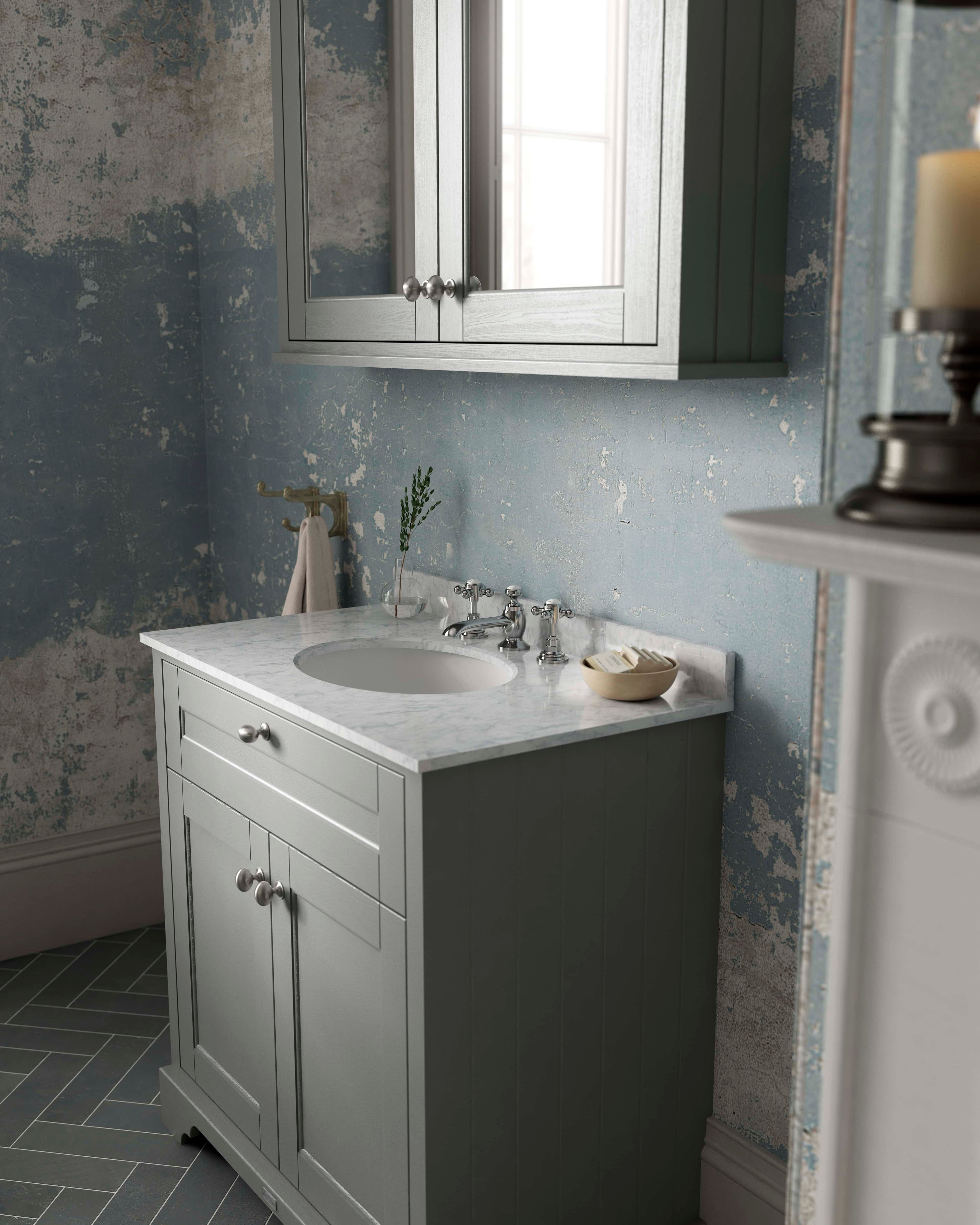 Natural grey bathroom vanity with white marble countertop and traditional plumbing fixtures, set against a distressed blue wall, reflecting elegant and timeless bathroom design.