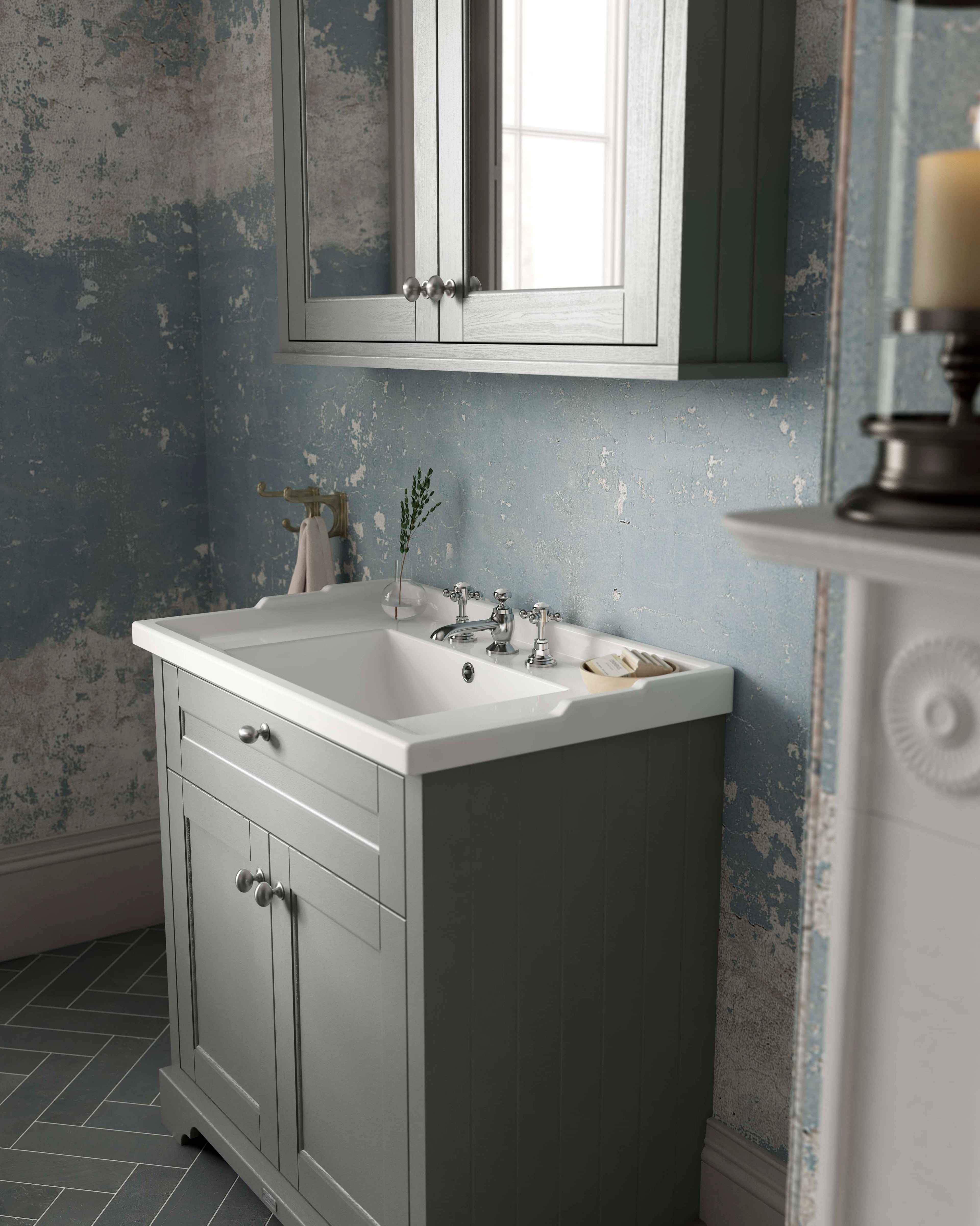 Elegant grey bathroom vanity with classic ceramic sink and chrome fixtures, surrounded by vintage distressed wallpaper and natural light from a nearby window, creating a stylish bathroom environment.