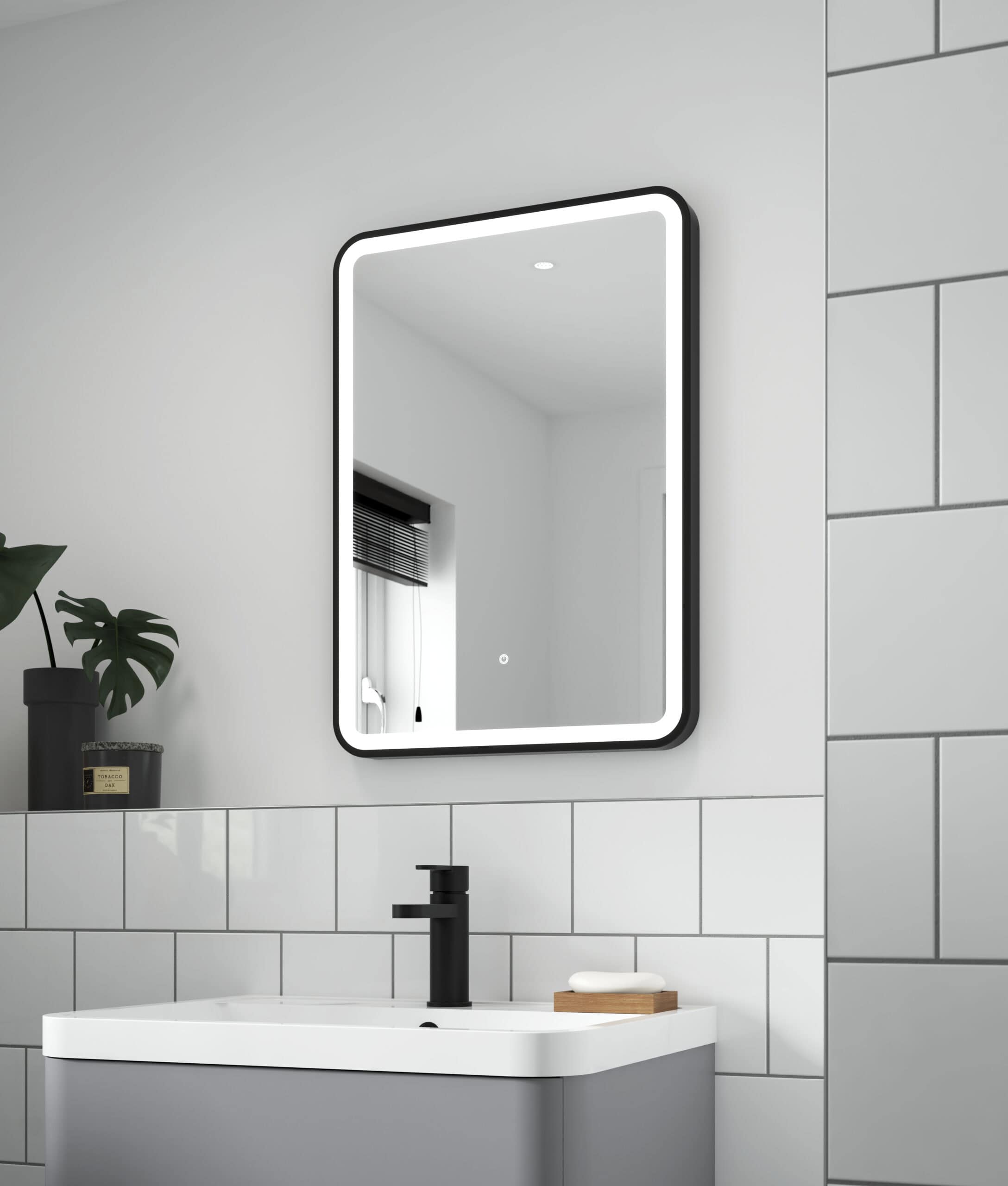 Sleek modern illuminated bathroom mirror with black frame above a contemporary white bathroom sink and black tap, minimalist bathroom decor with grey and white tiles, stylish bathroom design.