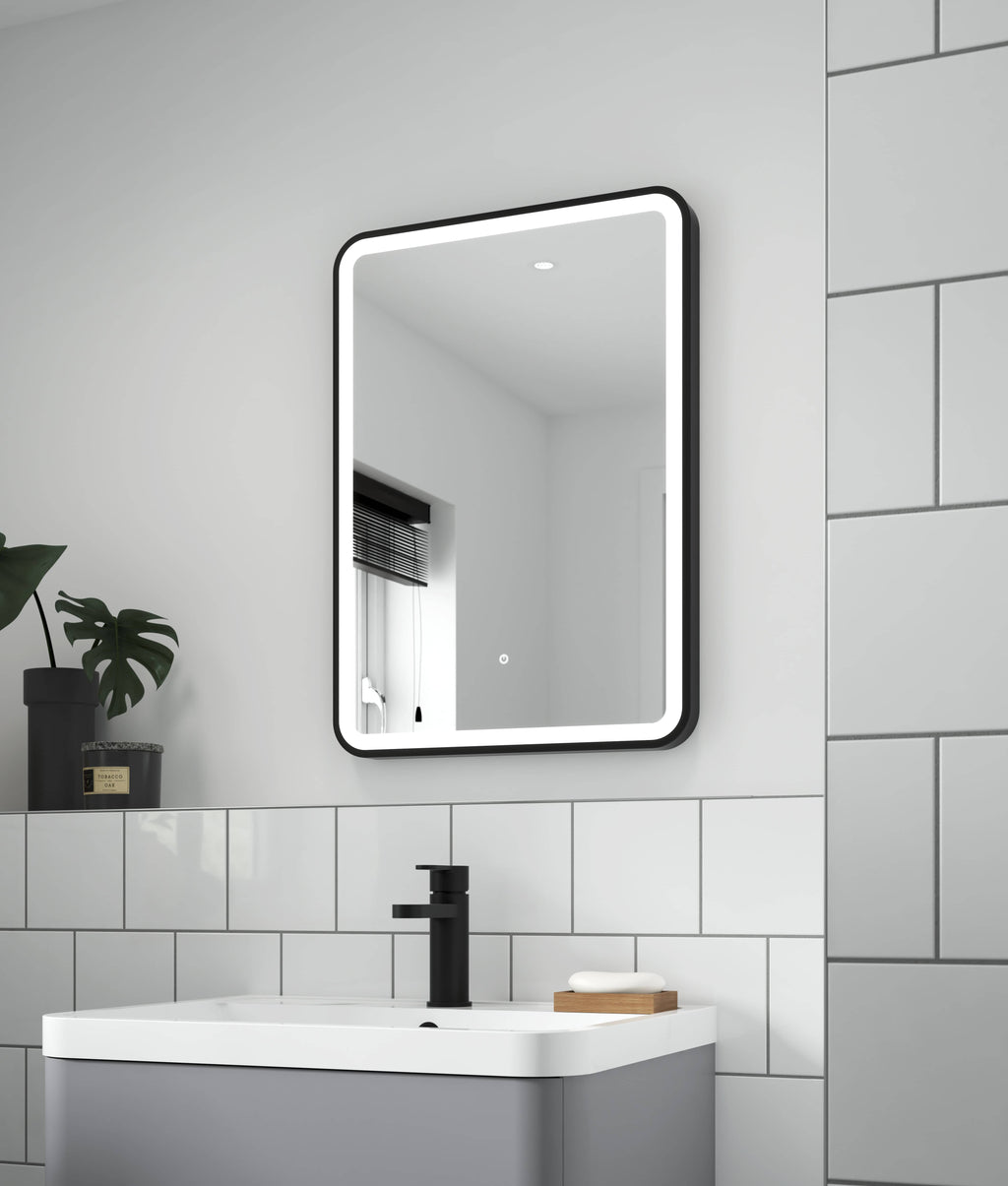 Modern illuminated black frame bathroom mirror in a contemporary bathroom setting with white tiles and sink.