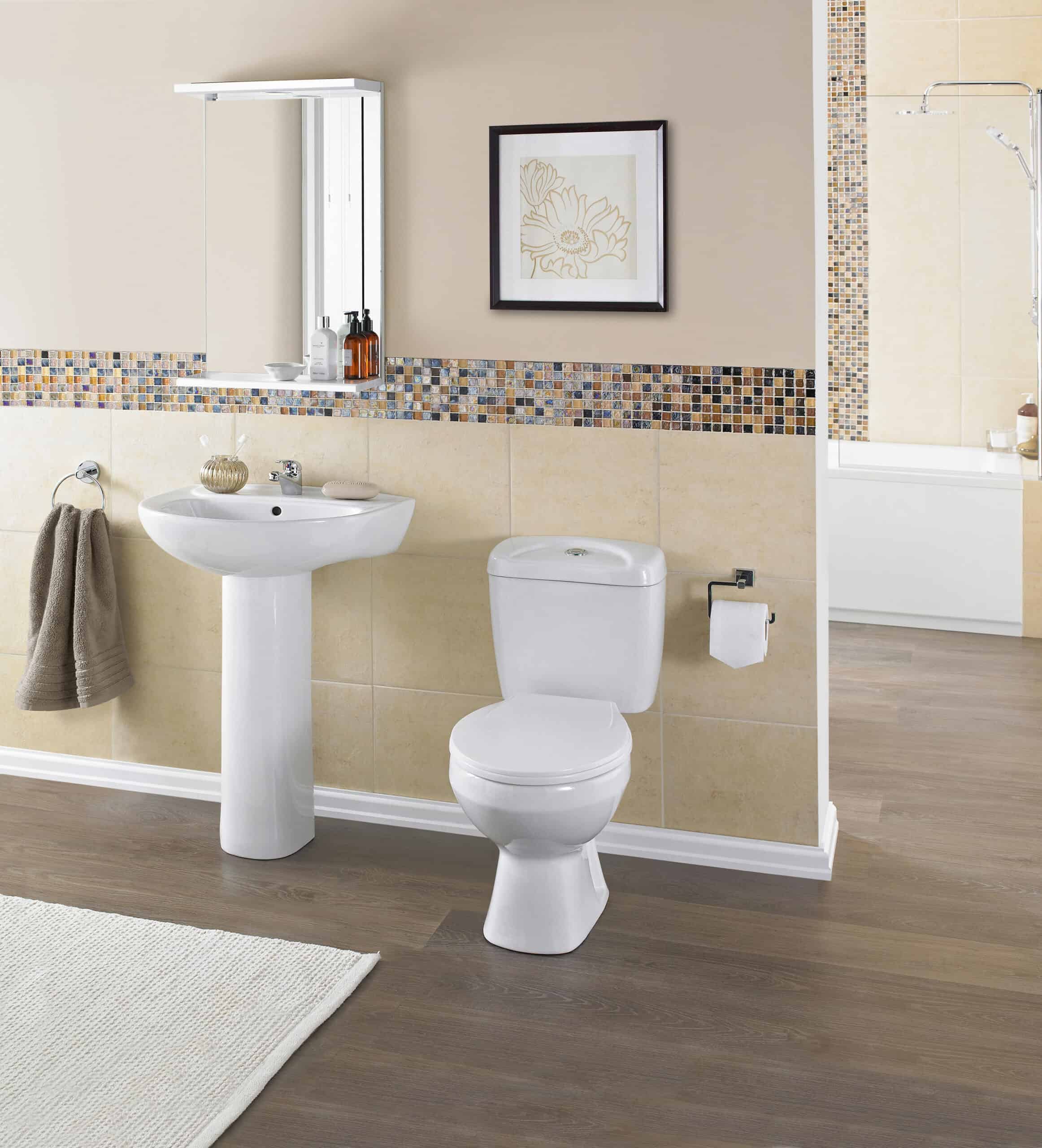 Modern bathroom with white ceramic toilet and pedestal sink, beige tiles with mosaic border, and bath area with shower, showcasing stylish and functional bathroom fixtures.