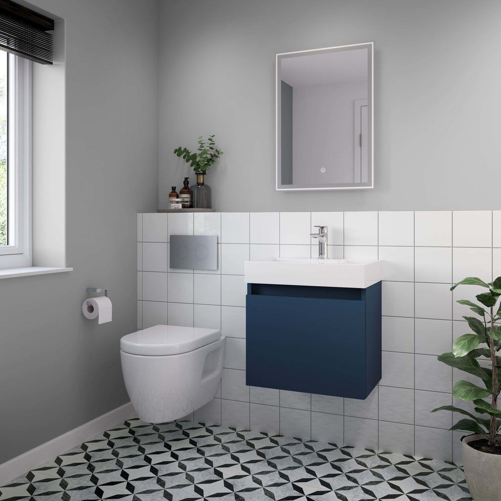 Modern bathroom with white toilet, navy vanity unit, wall-mounted mirror with LED lighting, black-and-white patterned floor tiles, and green potted plant in a minimalistic design.