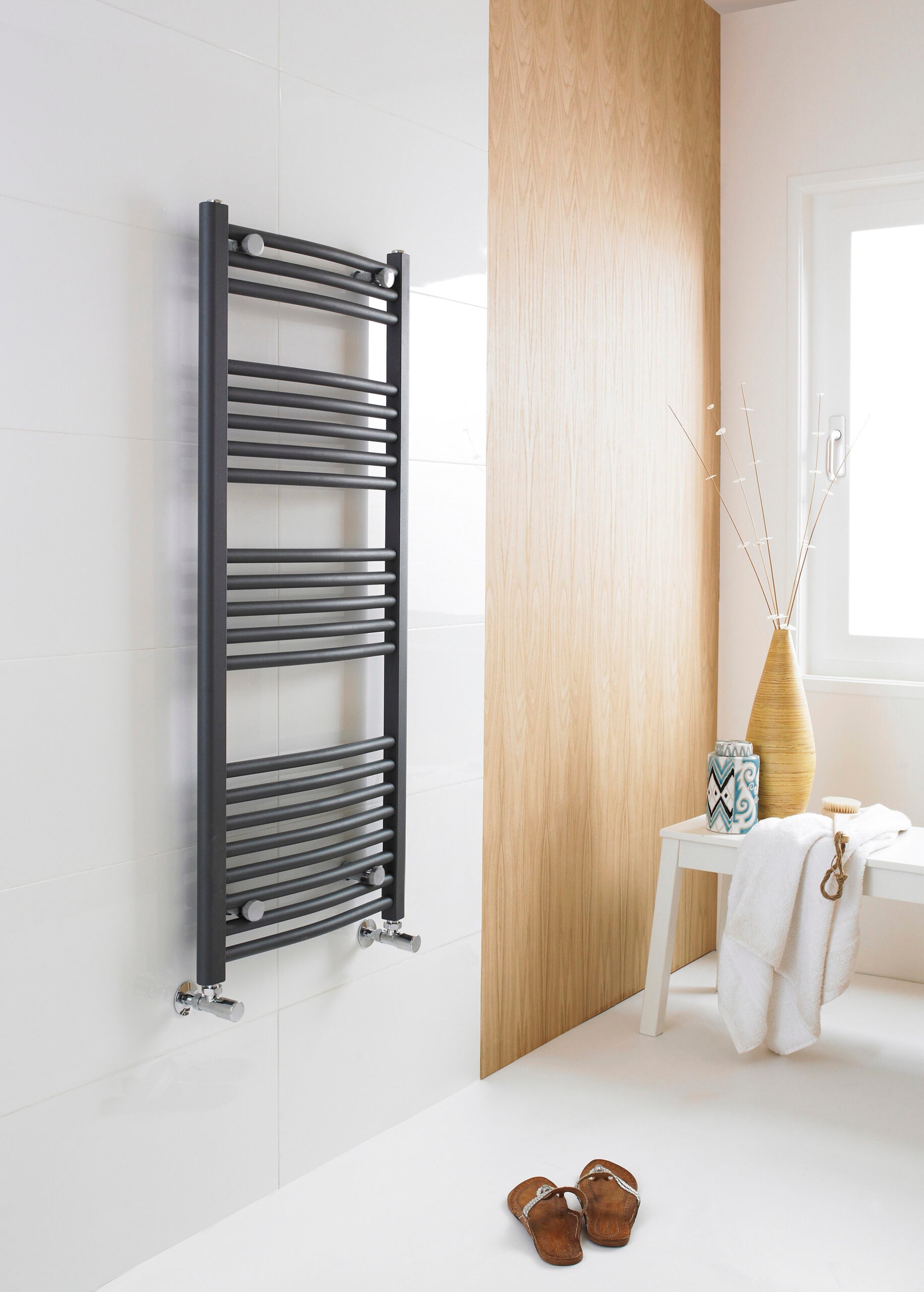 Sleek black towel radiator in modern bathroom with white tiled wall and natural wooden panel, minimalist decor, and drying towel; stylish heated towel rail for contemporary bathrooms.