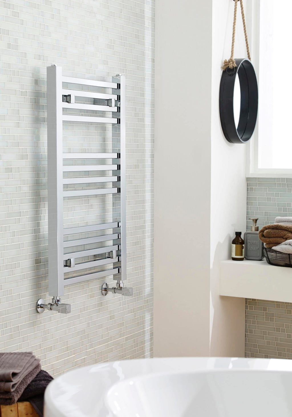 Polished stainless steel towel radiator in a modern bathroom with light tiled wall.