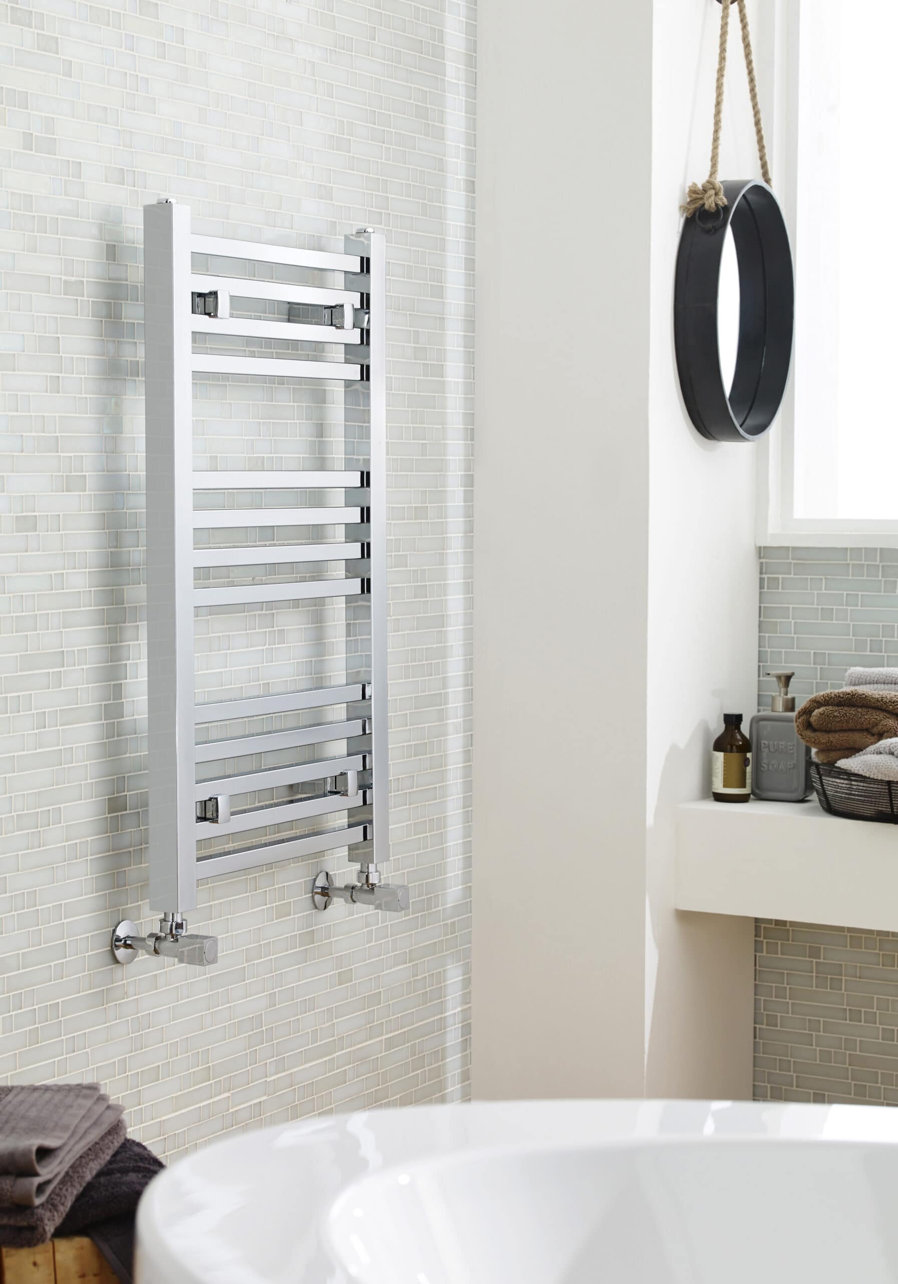 Polished stainless steel towel radiator in a modern bathroom with light tiled wall.