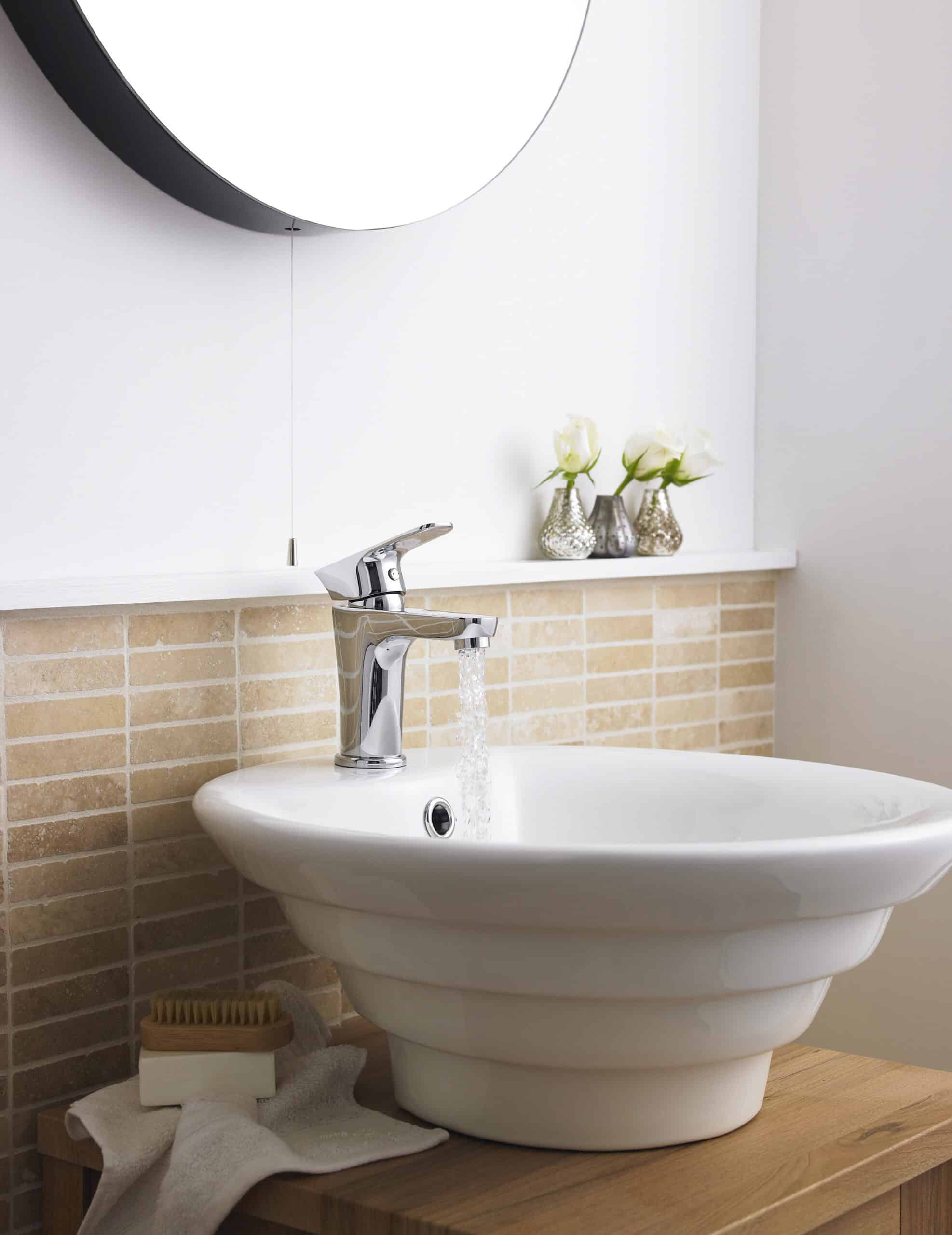 Elegant bathroom sink with chrome faucet, modern interior design, beige brick backsplash, and decorative flower vases, showcasing high-quality bathroom fixtures and stylish decor.