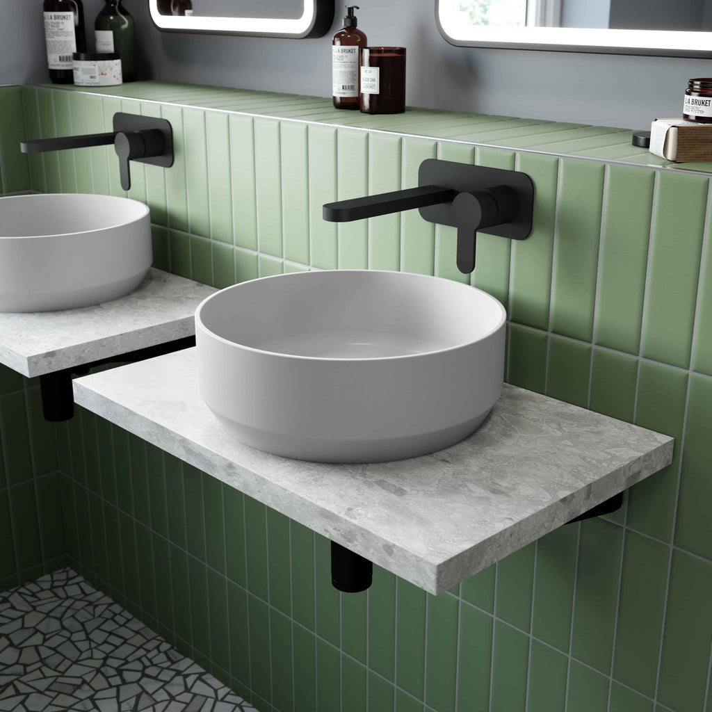 Vessel bathroom sink with black wall-mounted tap on green tiled wall in modern bathroom.