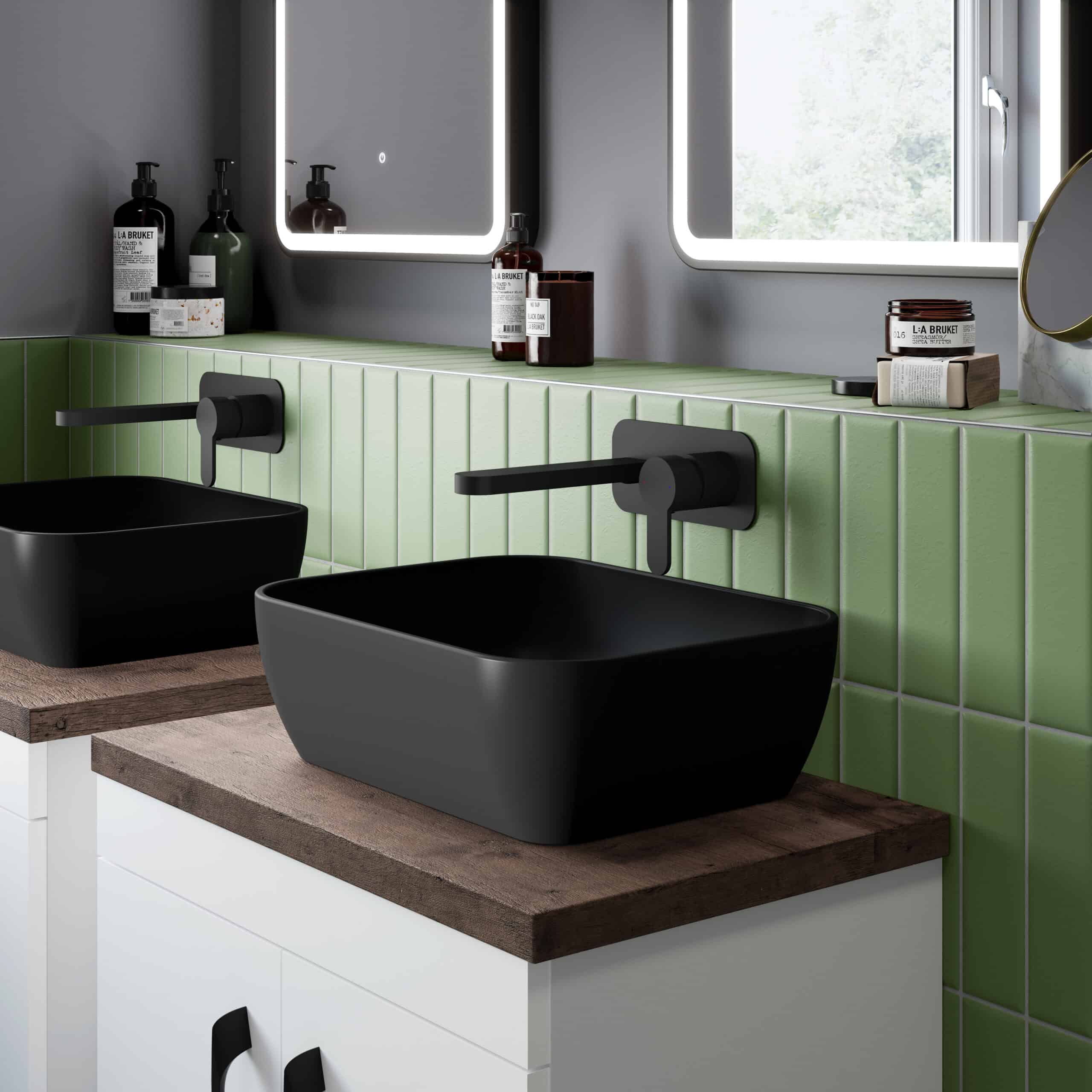 Sleek black bathroom washbasins with matte finish, wall-mounted black taps, and a stylish tiled green wall in a modern bathroom setting.