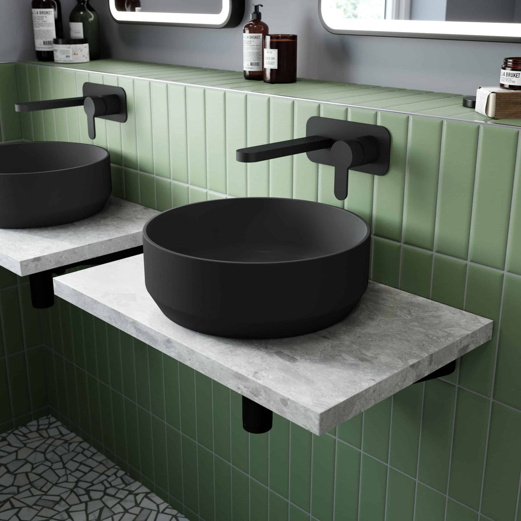 Black vessel sinks with modern black wall-mounted taps in a contemporary bathroom with green tiled wall and stone countertop.