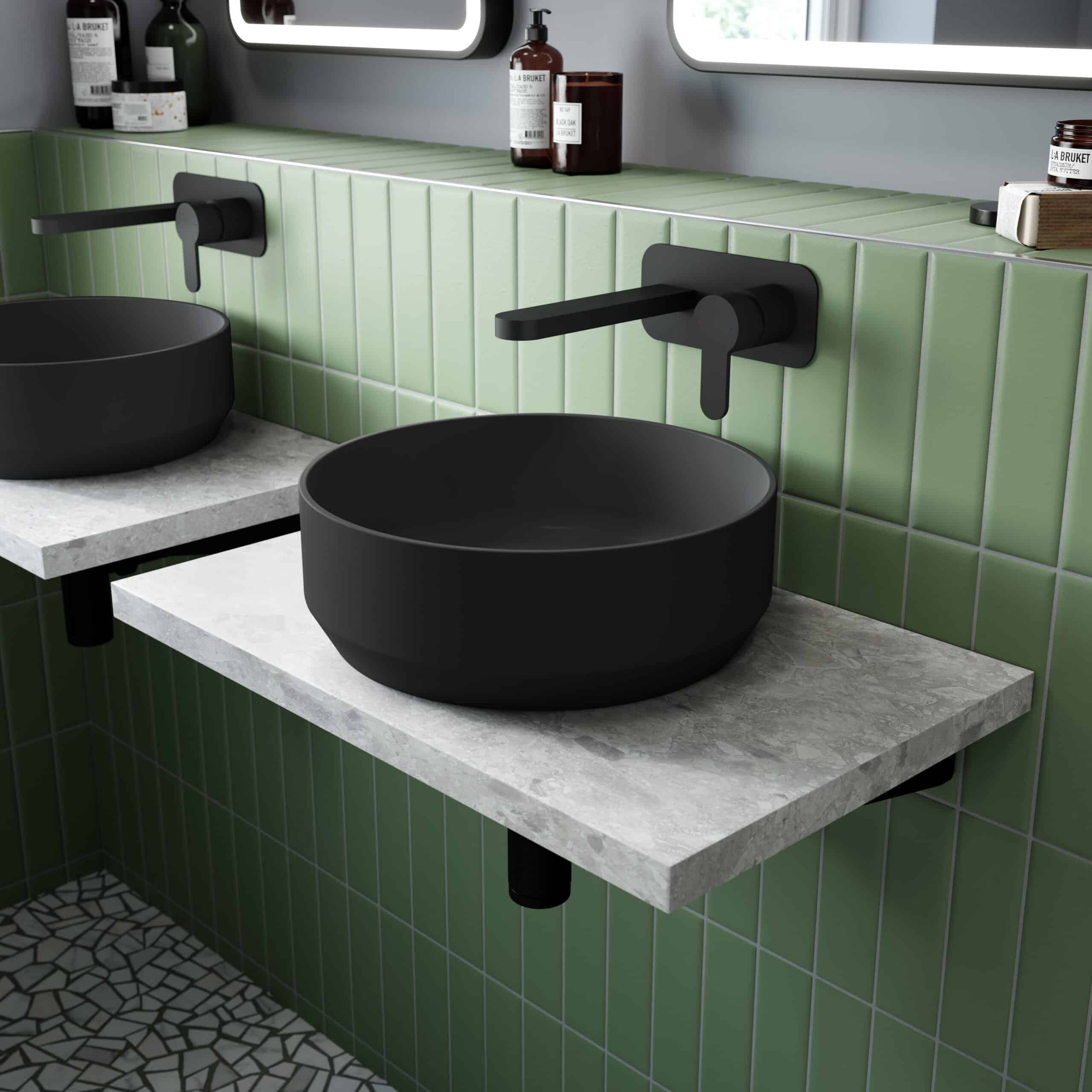 Black vessel sinks with modern black wall-mounted taps in a contemporary bathroom with green tiled wall and stone countertop.
