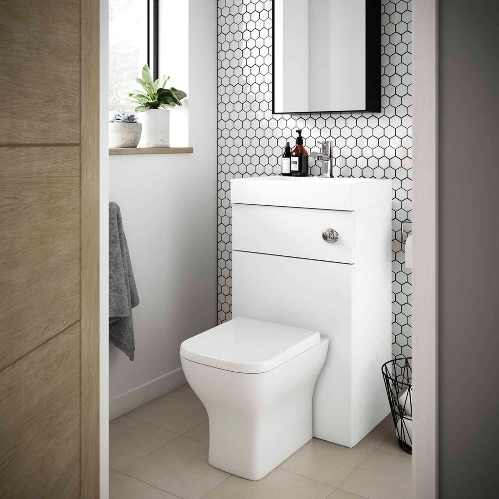 Contemporary bathroom with a modern white toilet and vanity unit, black and white hexagonal tiled accent wall, and a small window with a potted plant, showcasing stylish bathroom design.