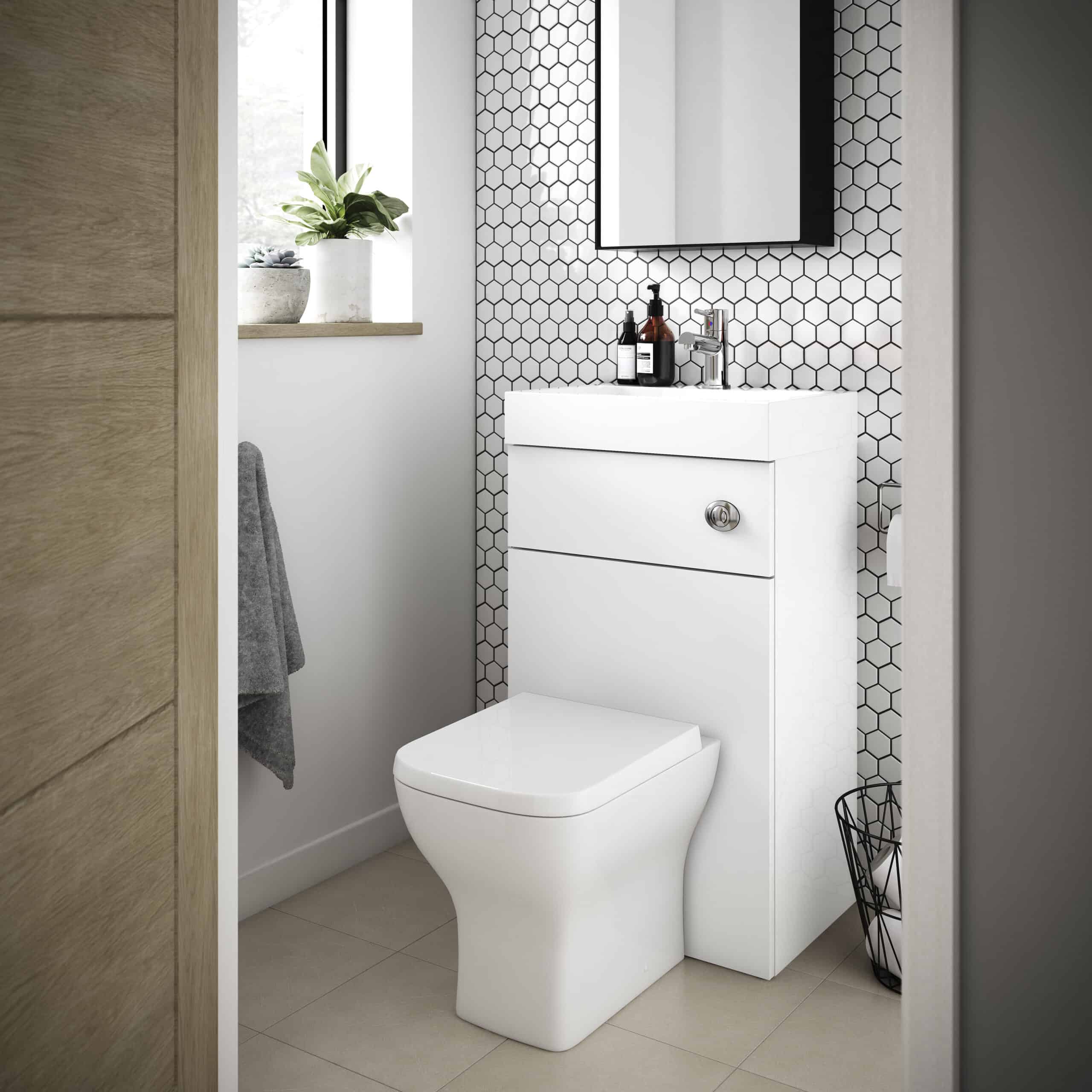 Contemporary bathroom with a modern white toilet and vanity unit, black and white hexagonal tiled accent wall, and a small window with a potted plant, showcasing stylish bathroom design.