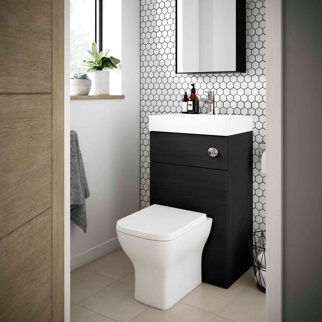 Modern bathroom with wall-mounted vanity and hexagonal tile accent wall, featuring a sleek white toilet and stylish black wood cabinet, complemented by a small potted plant and minimalist accessories for contemporary comfort.