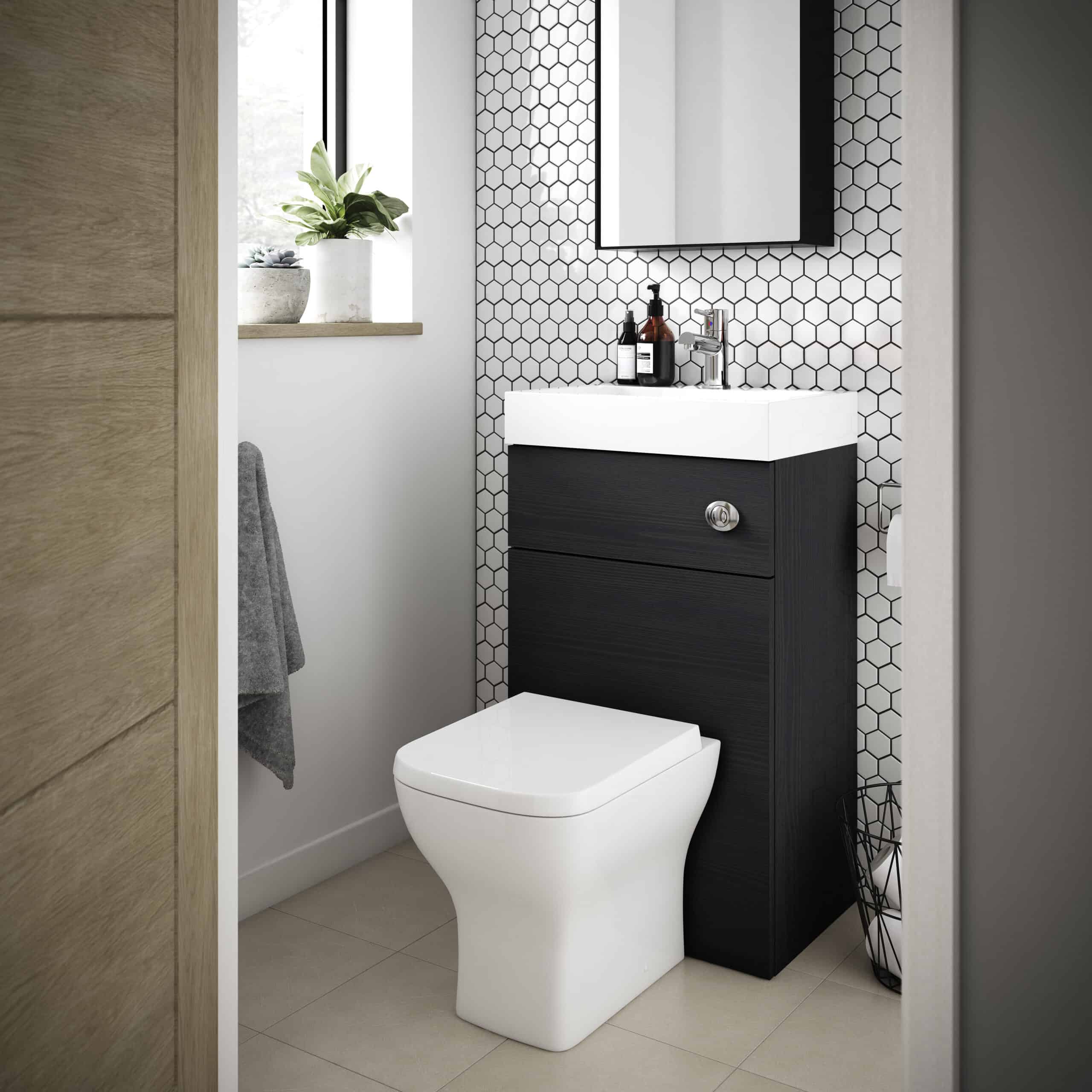 Modern bathroom with wall-mounted vanity and hexagonal tile accent wall, featuring a sleek white toilet and stylish black wood cabinet, complemented by a small potted plant and minimalist accessories for contemporary comfort.