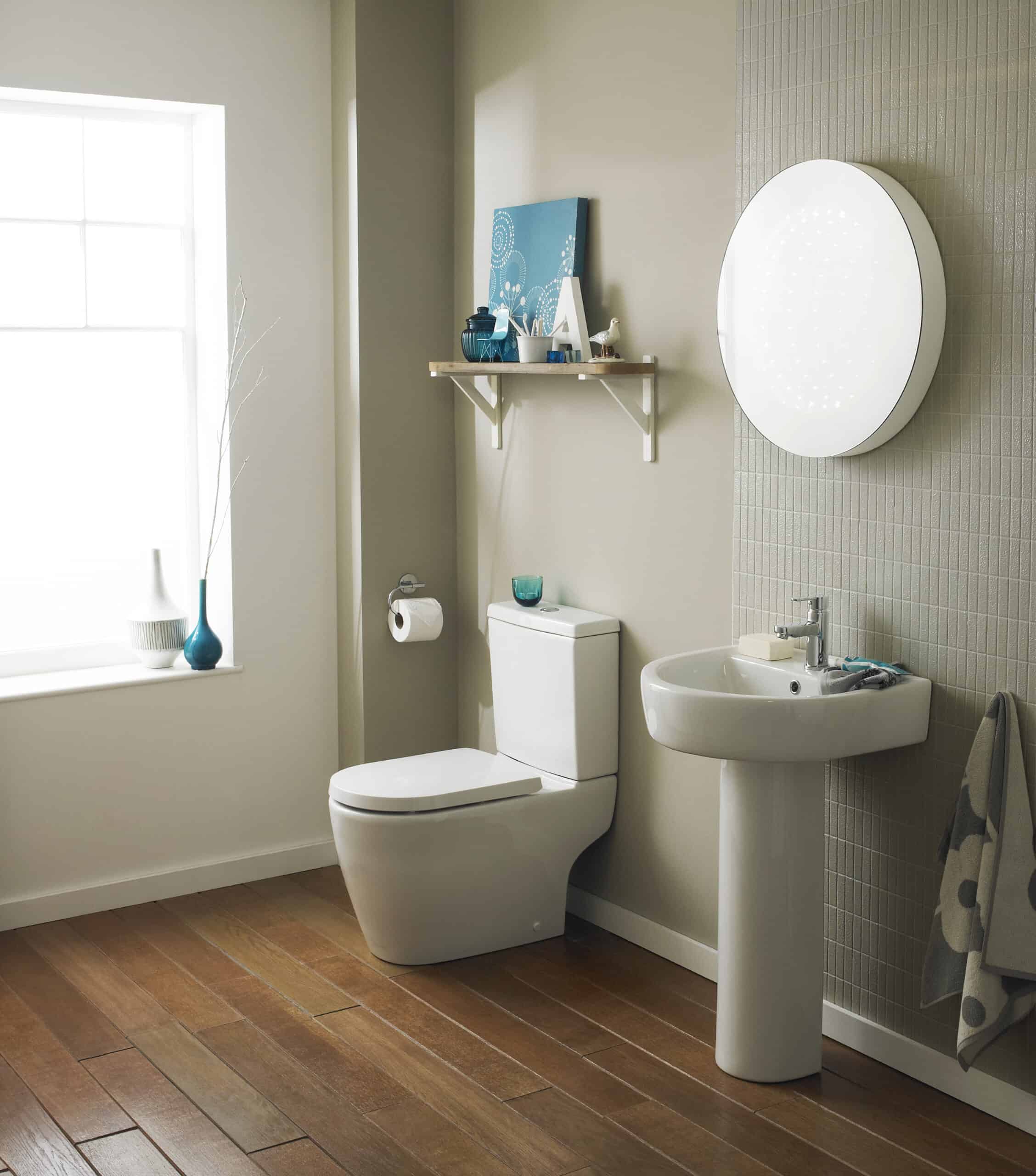 Sleek modern bathroom with white toilet and pedestal sink, beige tiled accent wall, and natural light from a large window, perfect for contemporary bathroom design.