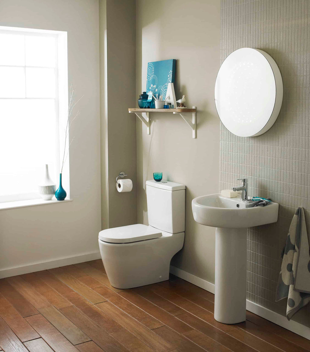 Sleek modern bathroom with white toilet and pedestal sink, beige tiled accent wall, and natural light from a large window, perfect for contemporary bathroom design.