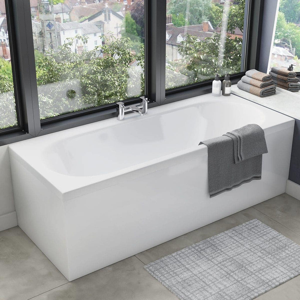 A modern white bathtub next to large windows with scenic outdoor views, decorated with neatly folded grey towels and bath essentials in a contemporary bathroom setting.