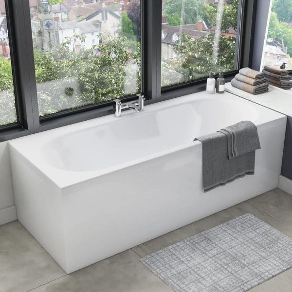 Modern freestanding white bathtub inside a contemporary bathroom with large windows and city view, grey towels and bath accessories, perfect for a relaxing bathing experience.