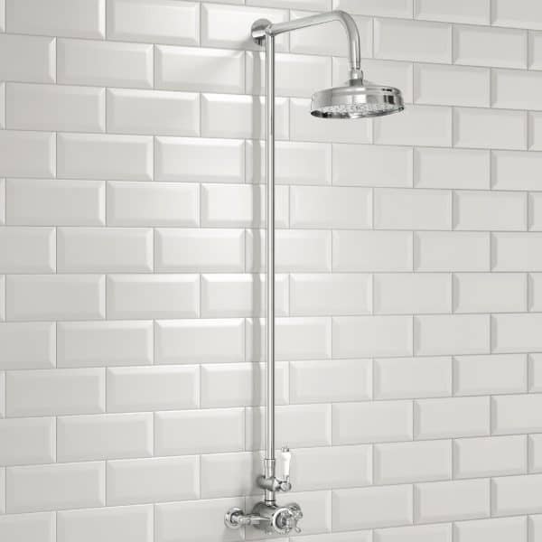 Shower head mounted on a sleek chrome pipe against a white subway tile wall in a modern bathroom.