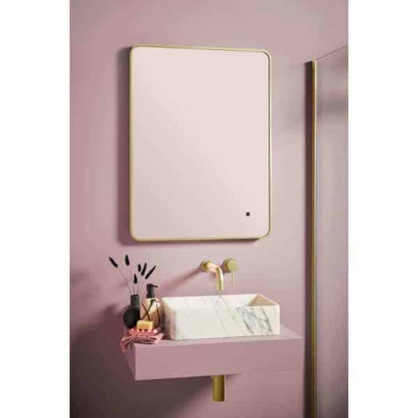 Pink bathroom vanity with marble sink and gold fixtures, minimalistic design featuring a wall-mounted mirror for modern bathroom decor.