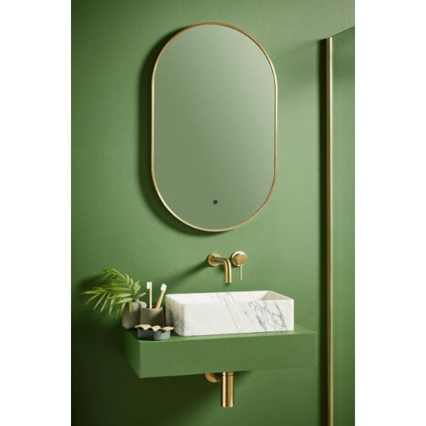 Oval mirror with gold trim above a modern green bathroom basin with gold fixtures, set against a matching green wall for a stylish, contemporary bathroom design.