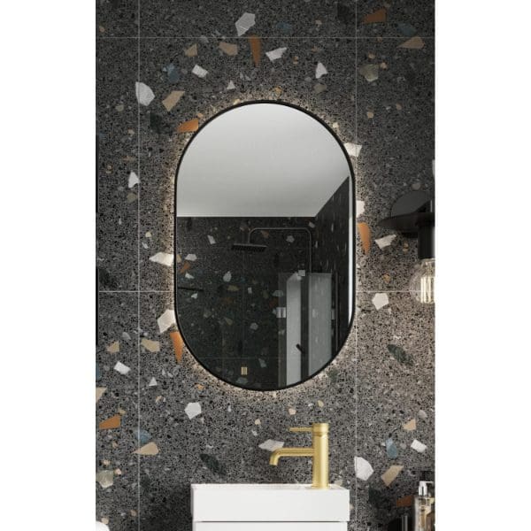 Reflective oval bathroom mirror with LED backlighting on a dark terrazzo wall in a modern bathroom.