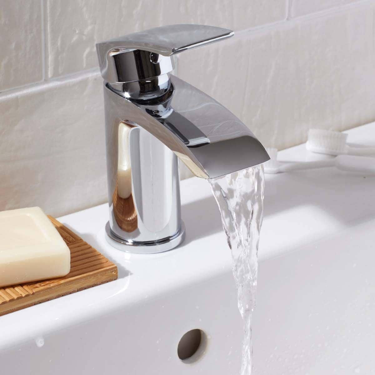 Shiny chrome bathroom faucet with running water on white ceramic sink, close-up.