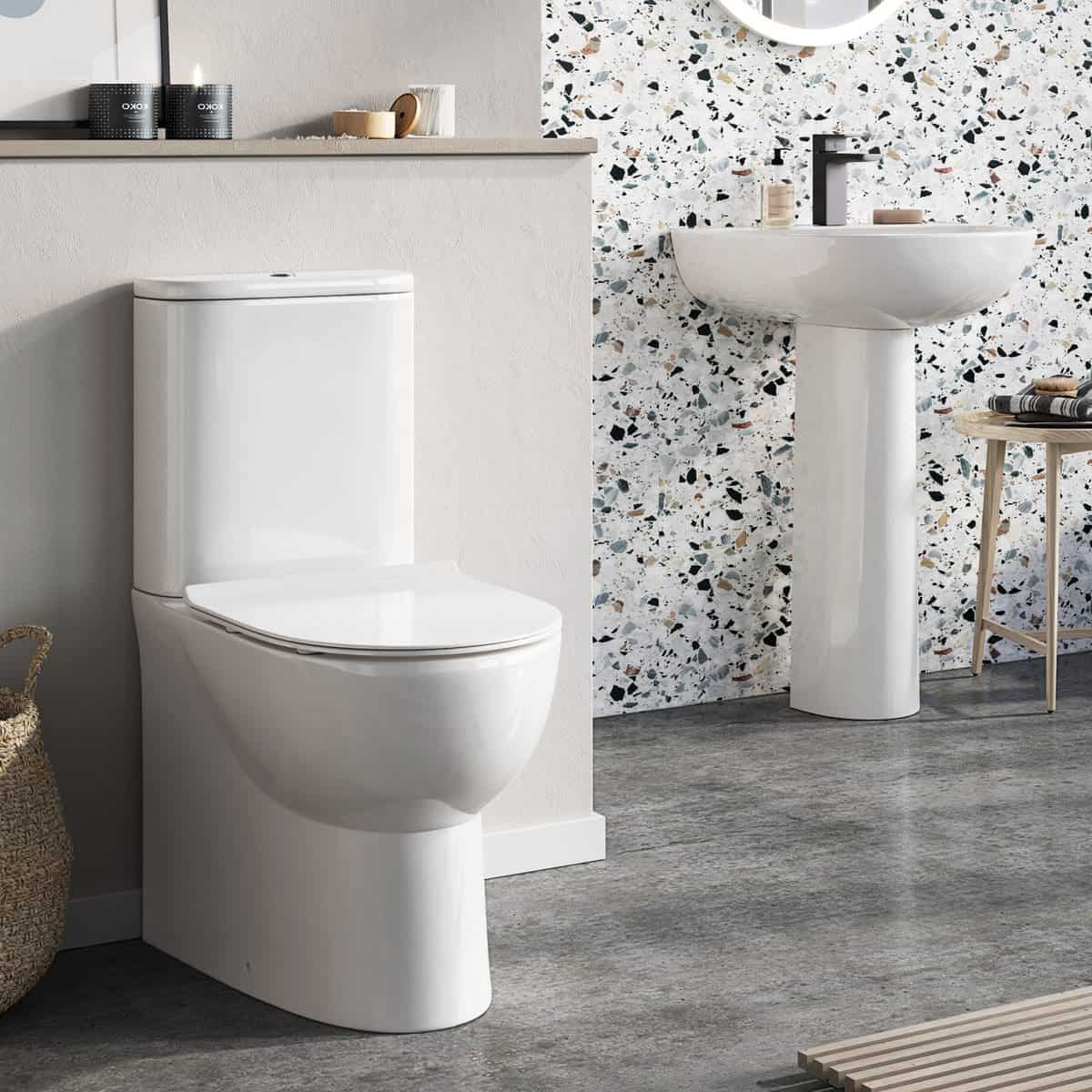 Sleek modern white toilet and pedestal sink in contemporary bathroom with terrazzo wall tiles, minimalist decor, and natural accents, ideal for stylish bathroom renovations and upgrades.