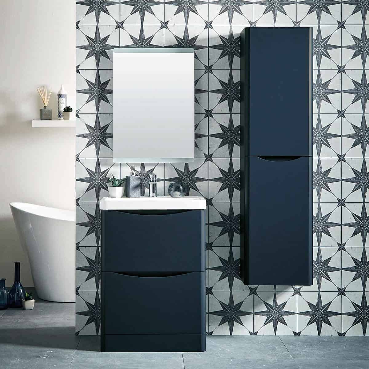 Modern navy bathroom vanity set with sleek storage drawers, matching tall cabinet, white countertop, and mirror with geometric tiled wall backdrop for stylish bathroom design.