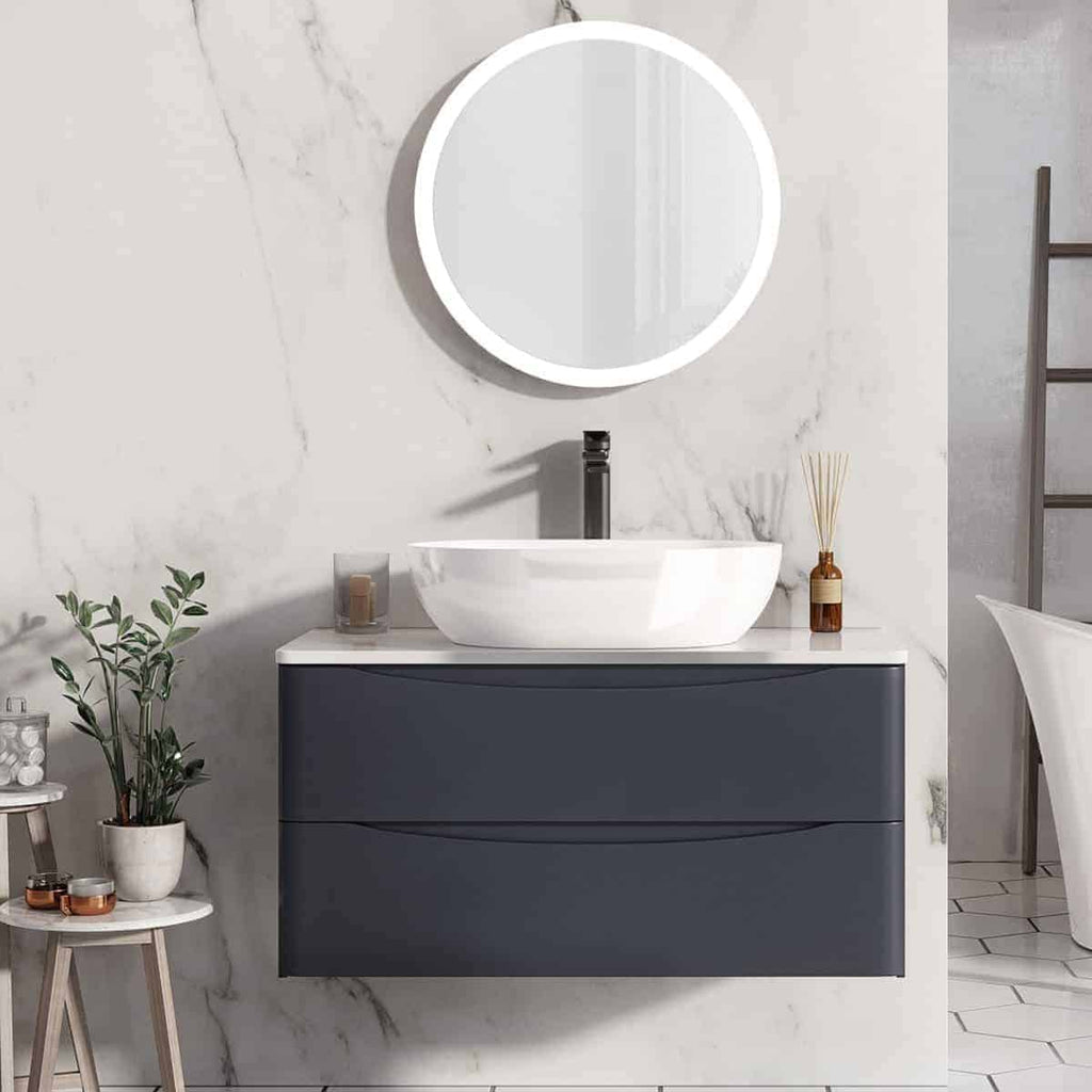Contemporary bathroom vanity featuring a sleek white vessel sink, modern black faucet, round backlit mirror, and minimalist decor on a marble wall backdrop.