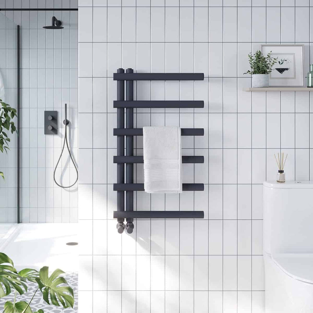 Radiator towel warmer in modern bathroom, black heatsource for towels, sleek bathroom heating appliance, stylish heated towel rail, contemporary bathroom radiator design with white tiled wall.