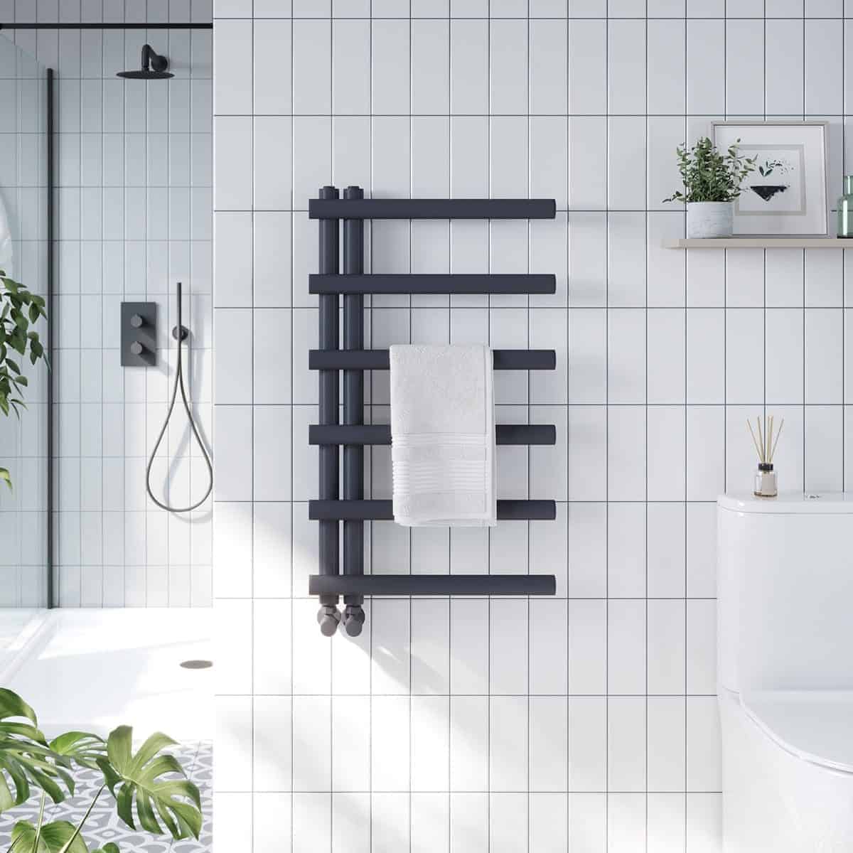 Radiator towel warmer in modern bathroom, black heatsource for towels, sleek bathroom heating appliance, stylish heated towel rail, contemporary bathroom radiator design with white tiled wall.