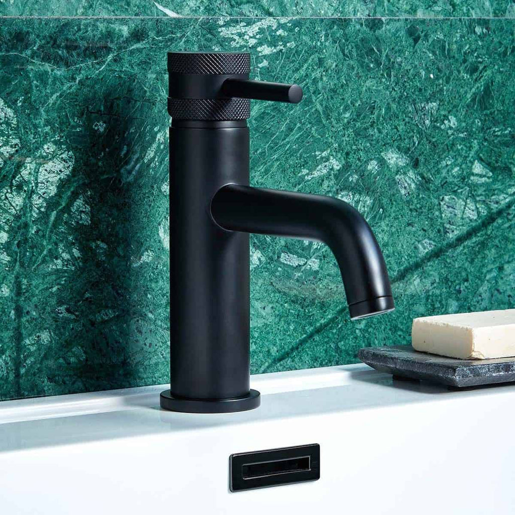 Sleek black bathroom tap with matte finish on a white sink, set against a luxurious green marble wall. Modern design, ideal for contemporary bathrooms seeking elegant fixtures.