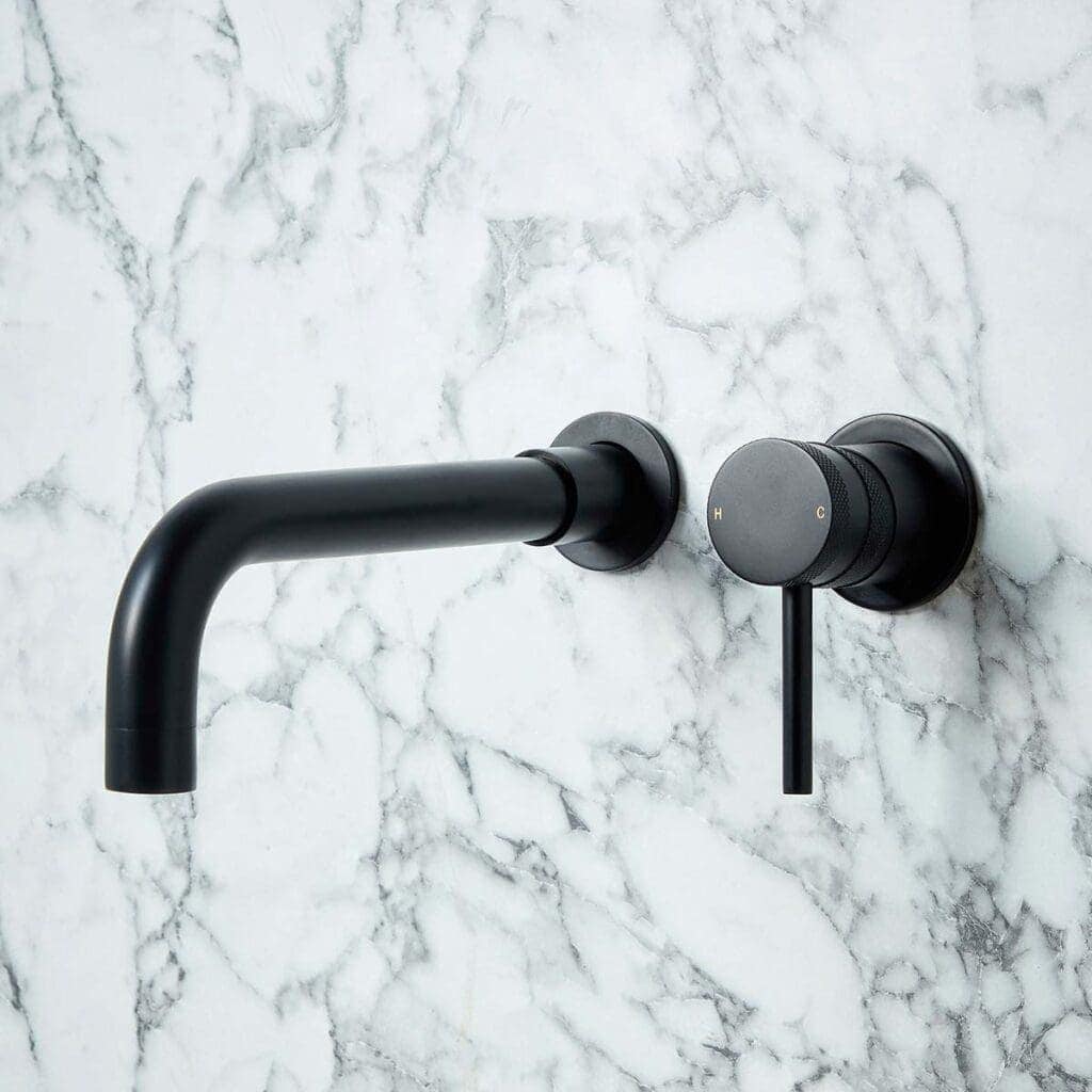 Modern black wall-mounted bathroom tap on a white marble wall, featuring sleek design and adjustable temperature control. Ideal for bathroom renovations and contemporary bathroom styles.