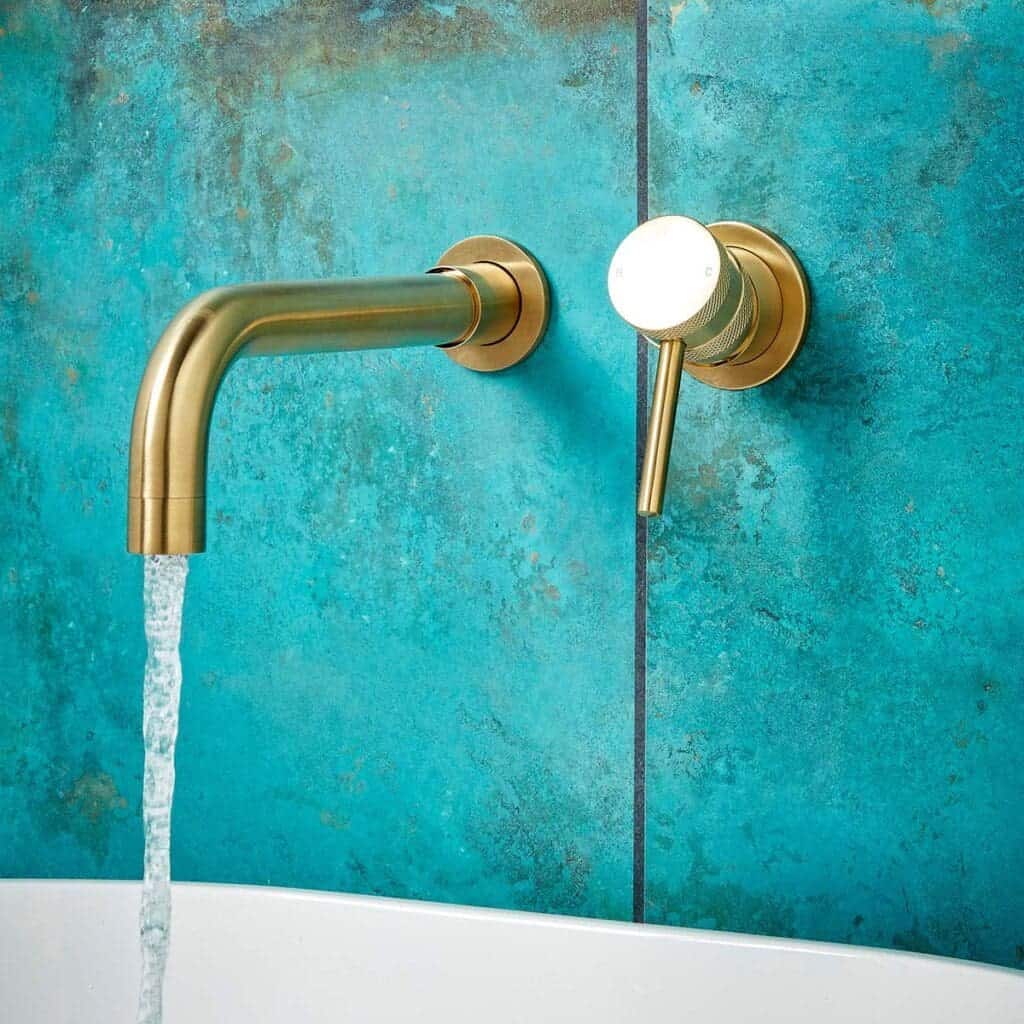 Sleek gold bathroom tap with modern design, mounted on vibrant turquoise wall, with water flowing in contemporary bathroom decor.