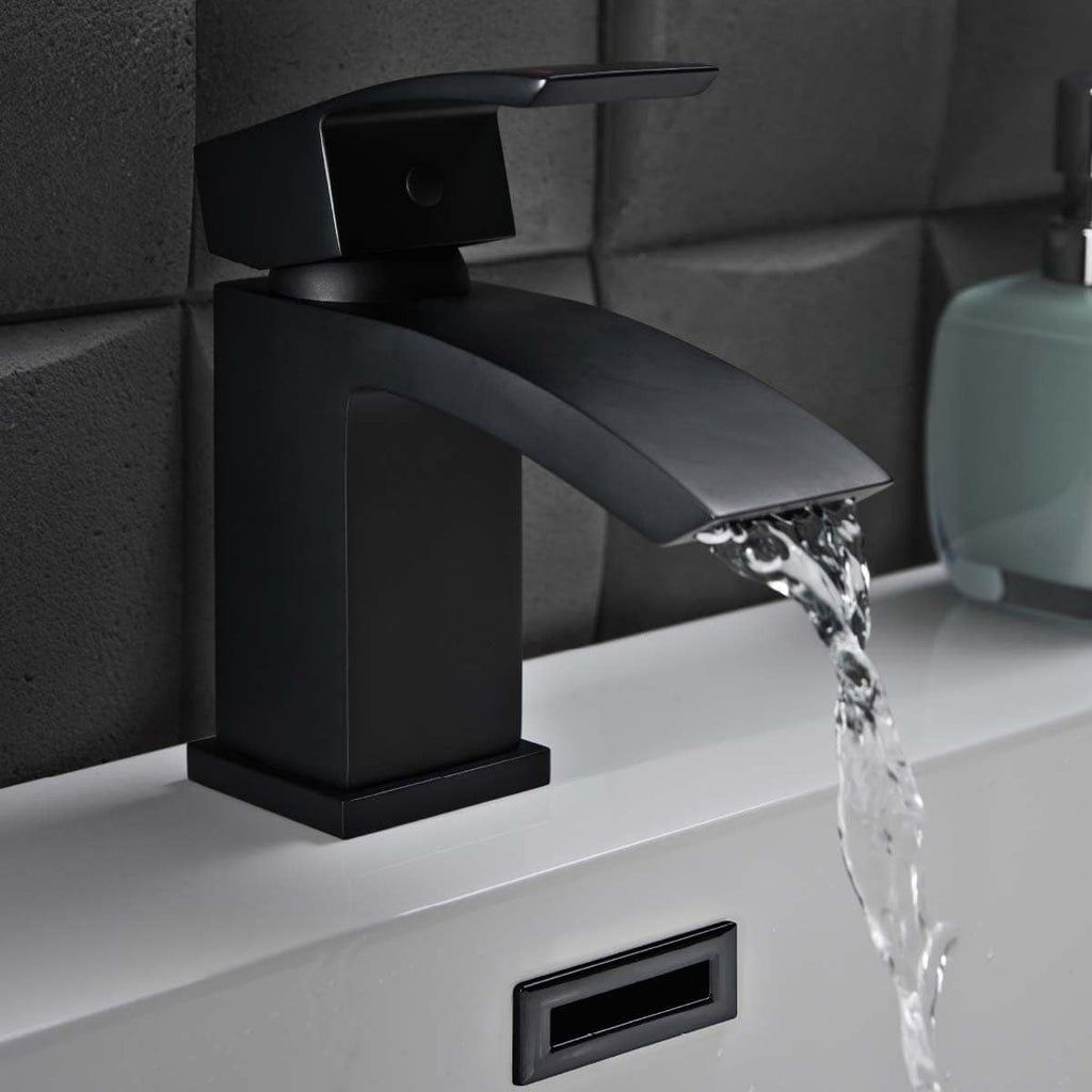 Sleek black bathroom faucet with waterfall spout water feature, modern design, installed on white bathroom sink with dark tiled wall background.