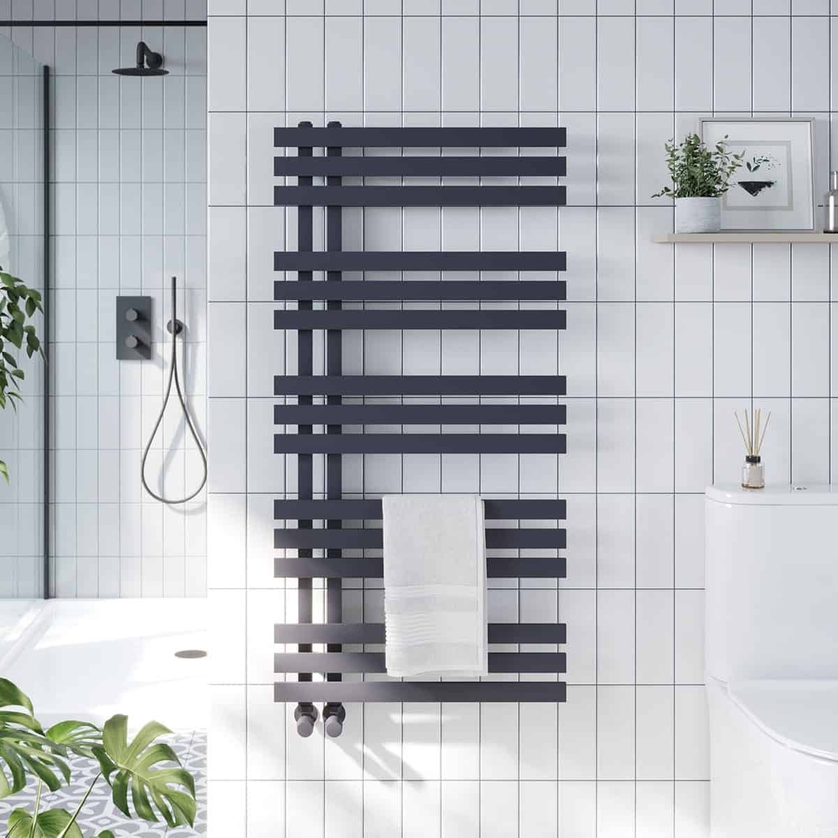 Radiator radiator towel warmer in modern black finish in a contemporary bathroom with white tiled walls and shower area.