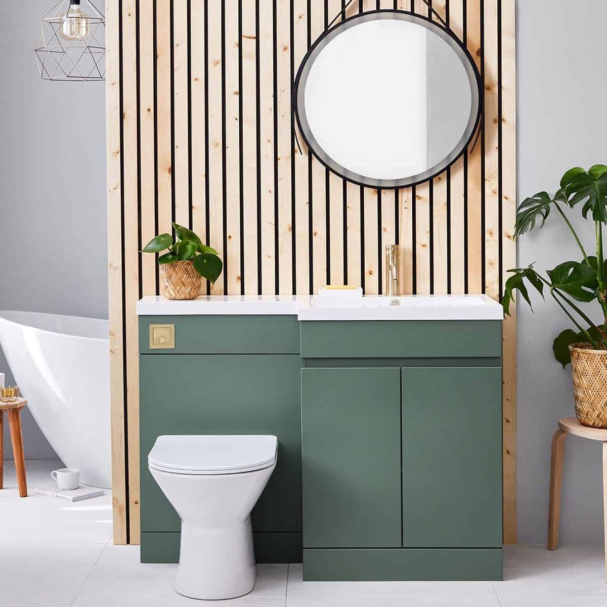 Modern green bathroom vanity with integrated toilet, stylish round mirror and decorative wooden wall panel, complemented by potted plants, blending contemporary and natural design elements for a relaxing bathroom space.