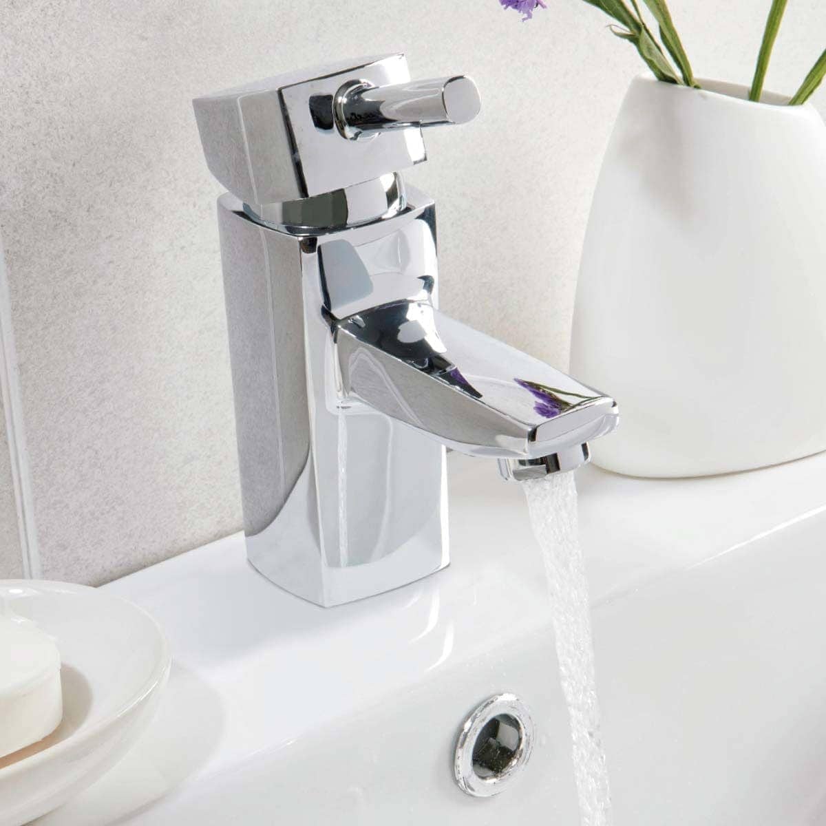 Shiny chrome bathroom tap with flowing water in a modern bathroom setting.