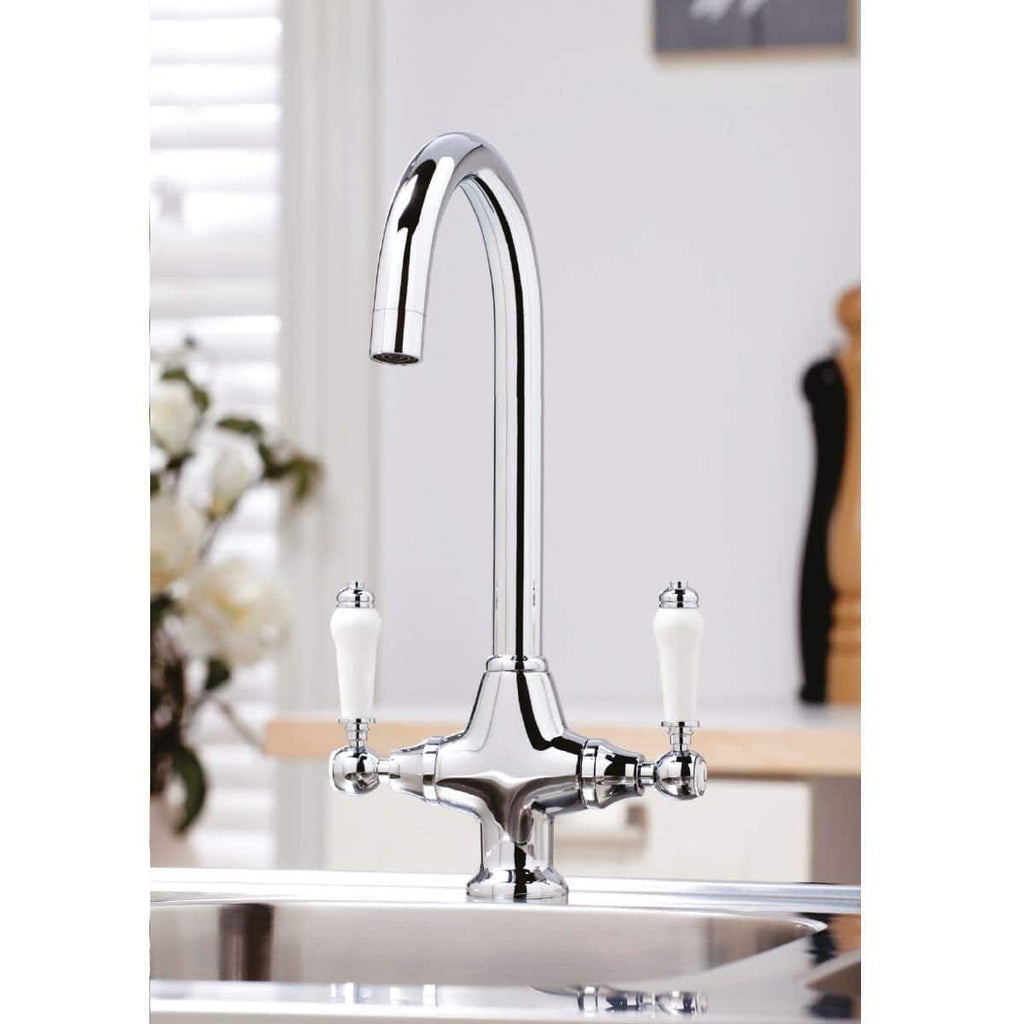 Polished chrome kitchen mixer tap with dual white ceramic handles, modern design, installed over stainless steel sink in contemporary bathroom setting.