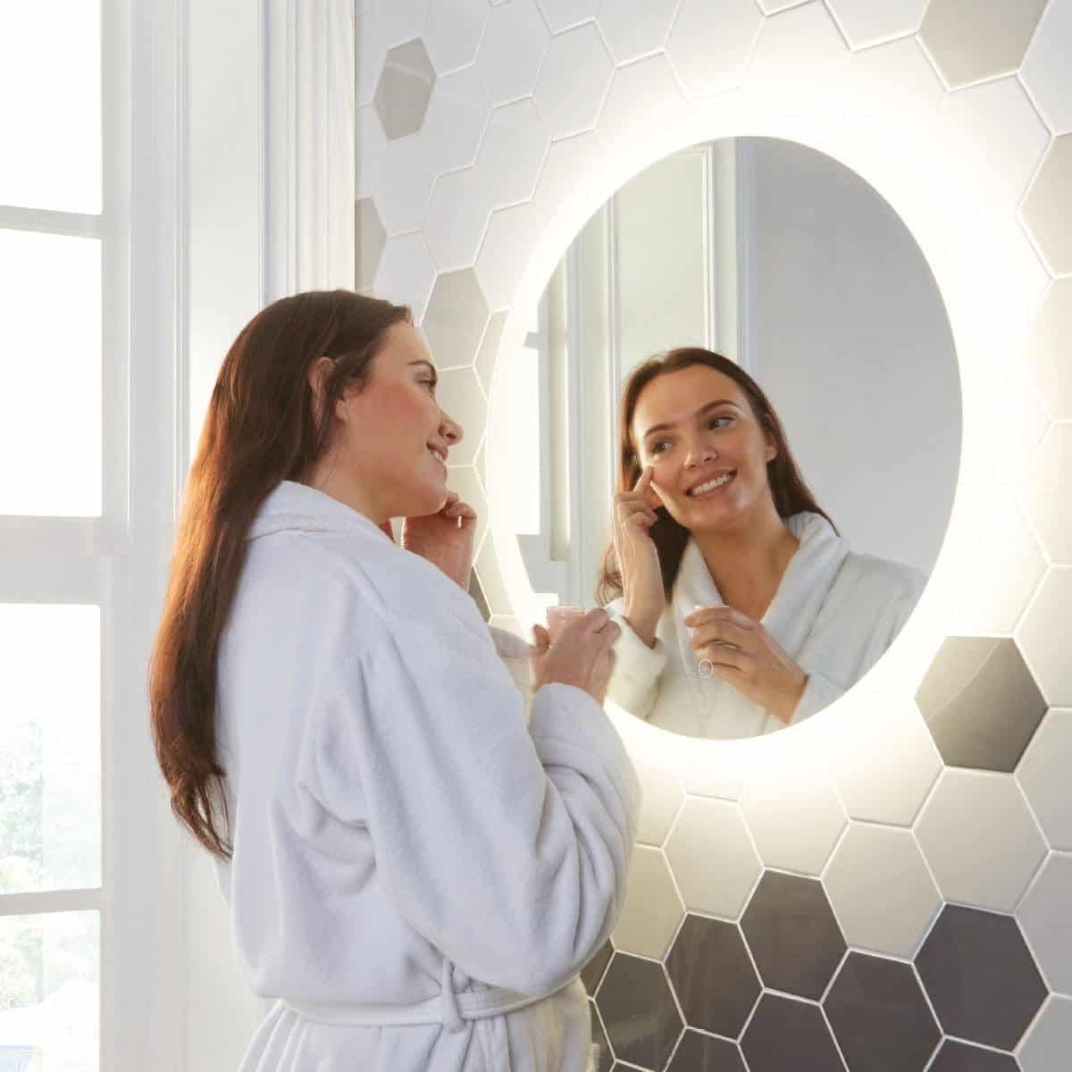 Showering woman admiring illuminated bathroom mirror with hexagon tiles for modern Bubly bathrooms aesthetic.
