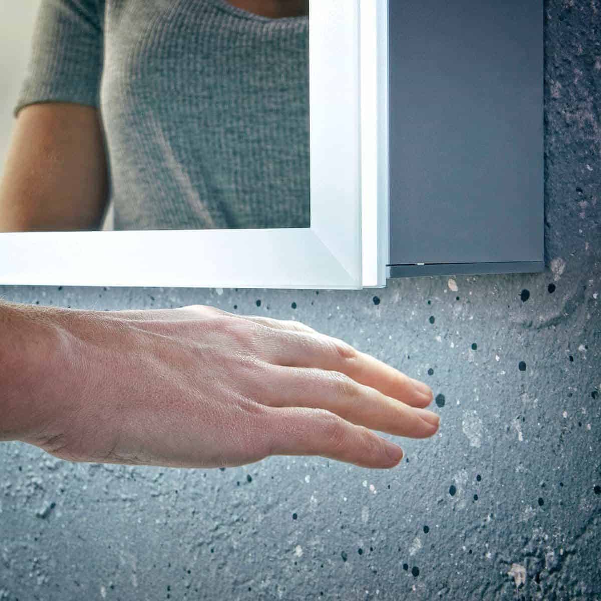 Sleek modern bathroom mirror with LED lighting and a hand touching the concrete countertop, showcasing contemporary design and bathroom vanity ideas for stylish interiors.