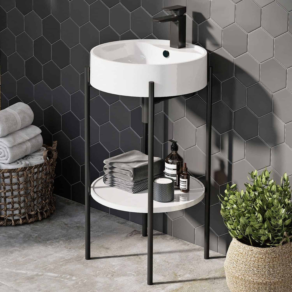 Elegant bathroom vanity with circular sink and black modern tap, featuring a two-tier storage shelf for toiletries, set against a stylish dark hexagonal tiled wall with greenery in a woven basket.