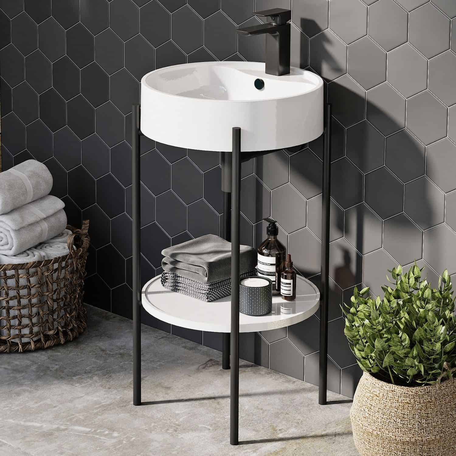 Elegant bathroom vanity with circular sink and black modern tap, featuring a two-tier storage shelf for toiletries, set against a stylish dark hexagonal tiled wall with greenery in a woven basket.