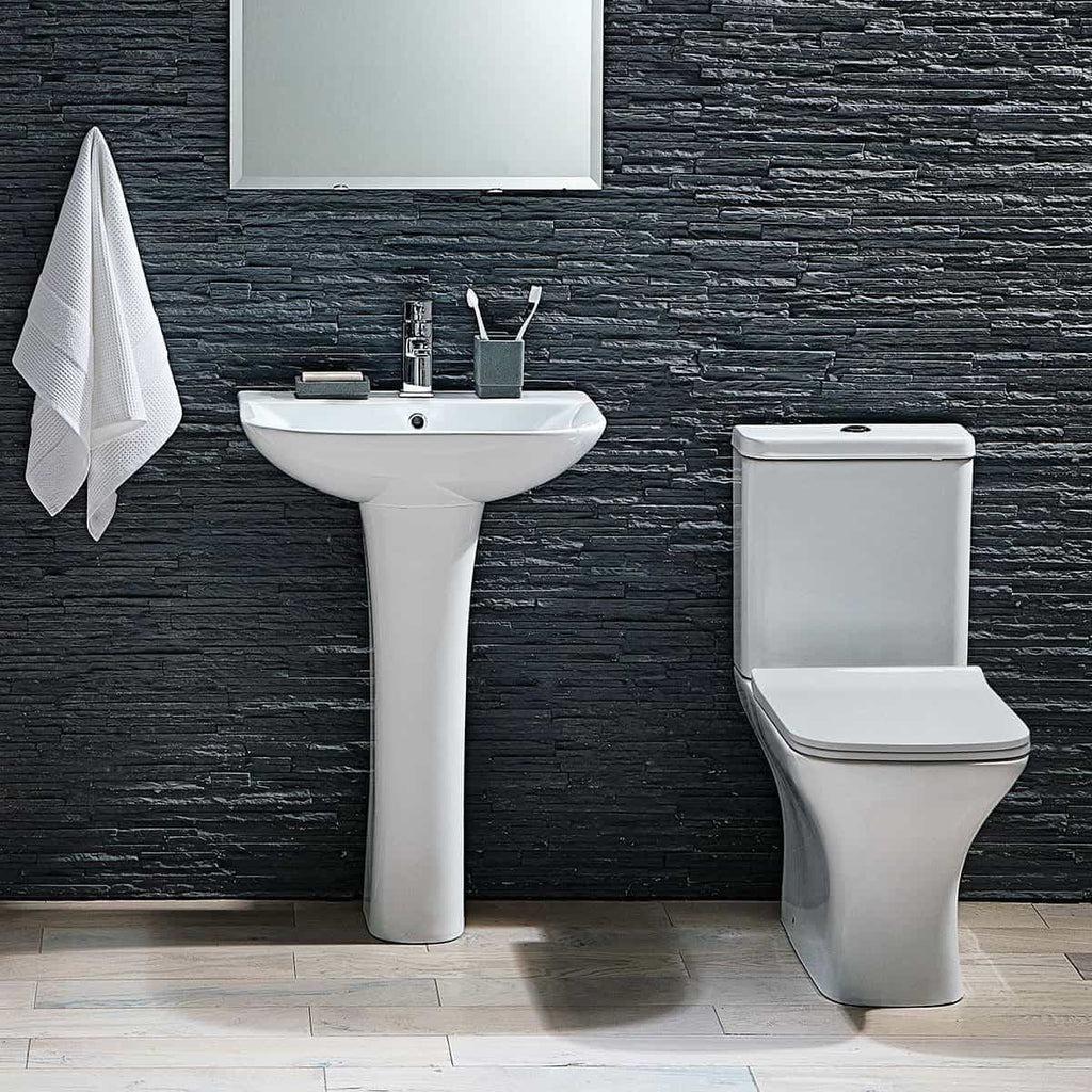 Sleek modern bathroom with white pedestal sink and close-coupled toilet set against a textured black stone wall, accessorised with hand towels and toiletries, exemplifying high-end bathroom design.